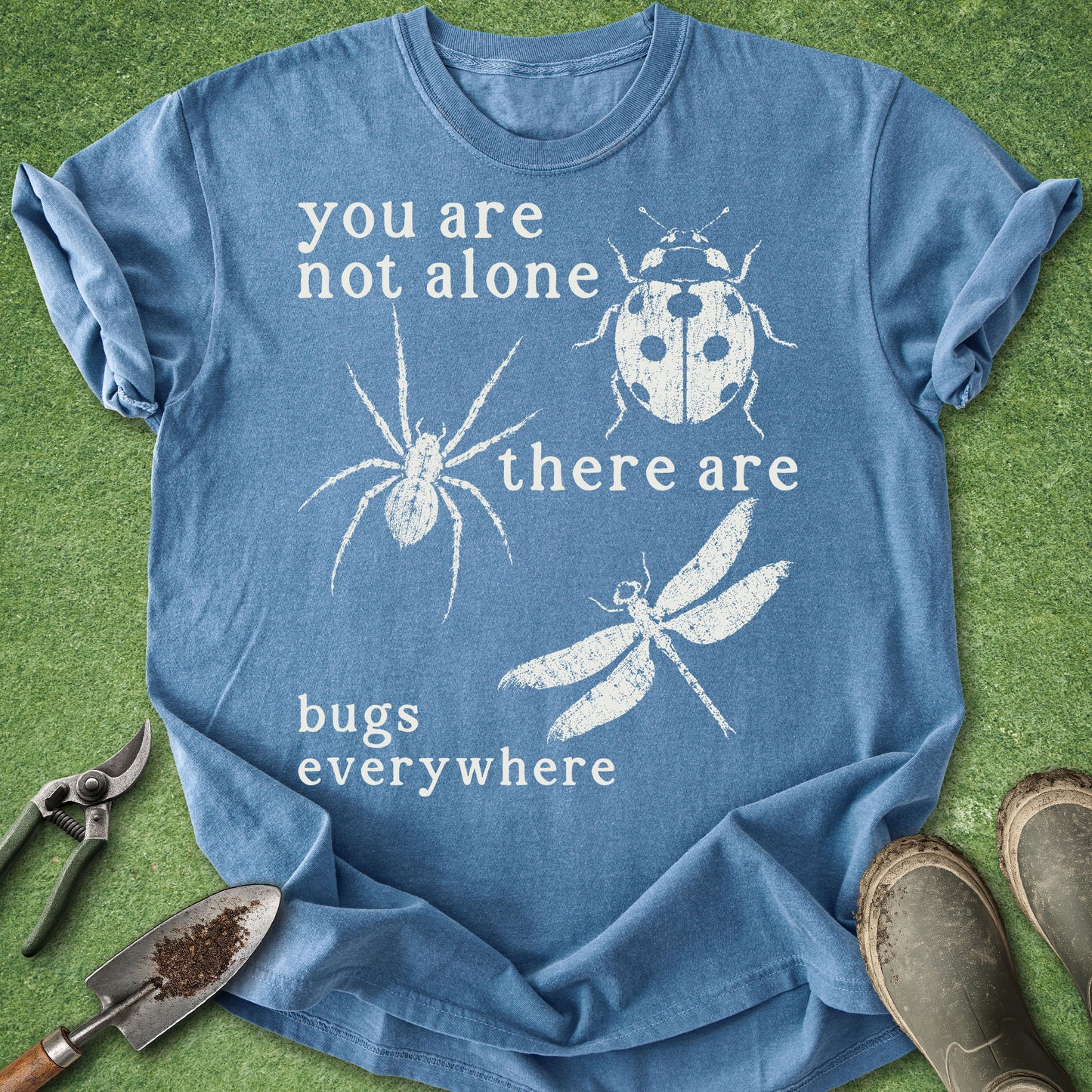 Blue t-shirt with white text and insect illustrations on a green grass background
