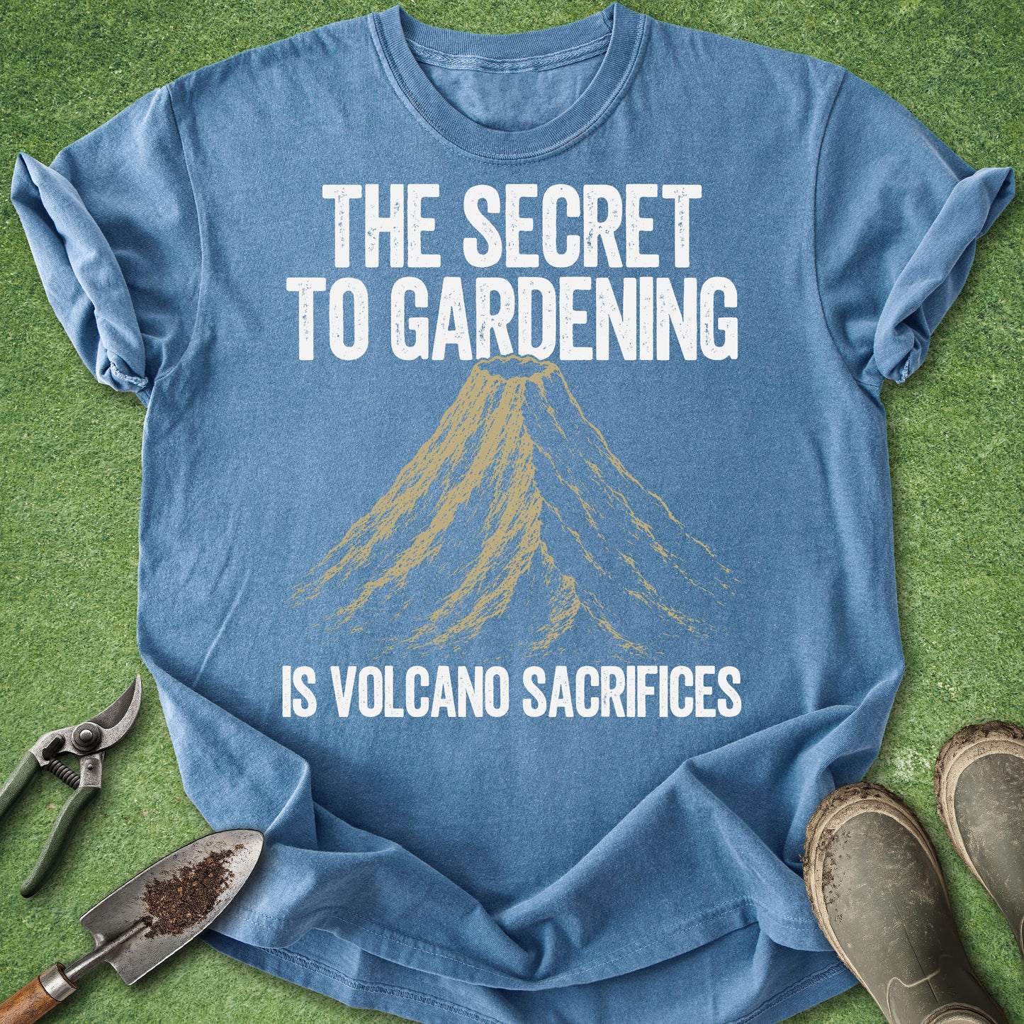 Comfort Colors blue t-shirt featuring a vintage volcano illustration with the humorous quote "The Secret to Gardening Is Volcano Sacrifices" in distressed white lettering.
