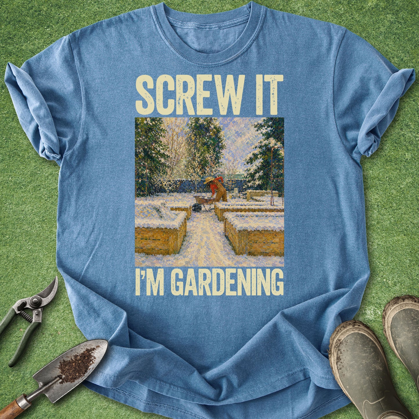 Blue t-shirt with 'Screw it, I'm gardening' text and garden-themed graphic on a grass background.