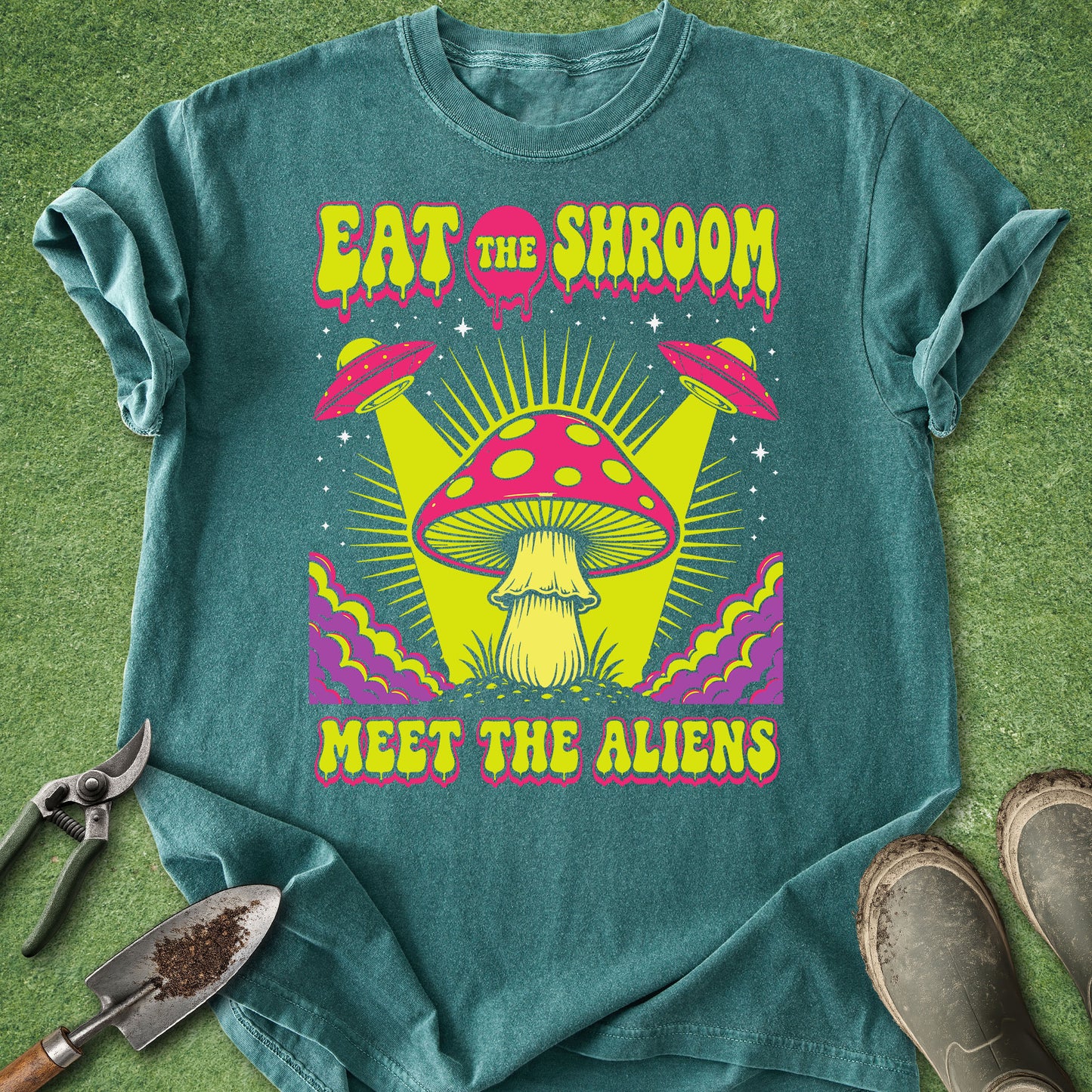 Comfort Colors blue spruce t-shirt featuring the phrase "Eat the Shroom Meet the Aliens" with a psychedelic mushroom, flying UFOs, neon colors, cosmic rays, and retro sci-fi artwork.