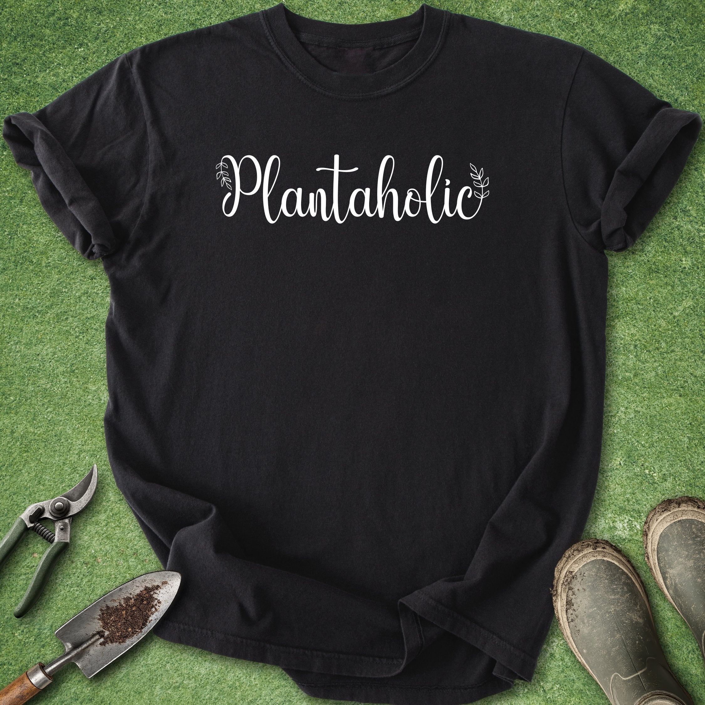 Black t-shirt with 'Plantaholic' text on a green grass background with gardening tools.