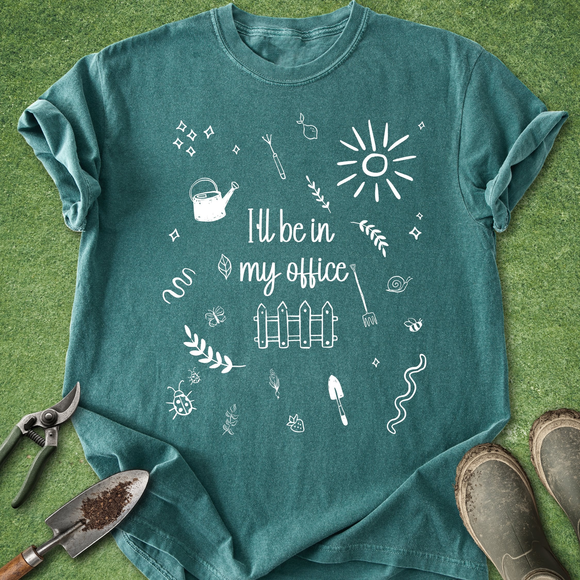 Teal t-shirt with white gardening-themed graphics and text on a grass background
