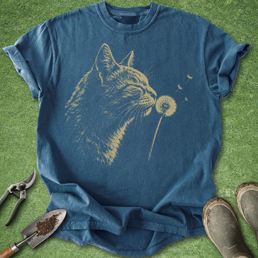 Blue t-shirt with a cat blowing on a dandelion graphic on a grassy background.