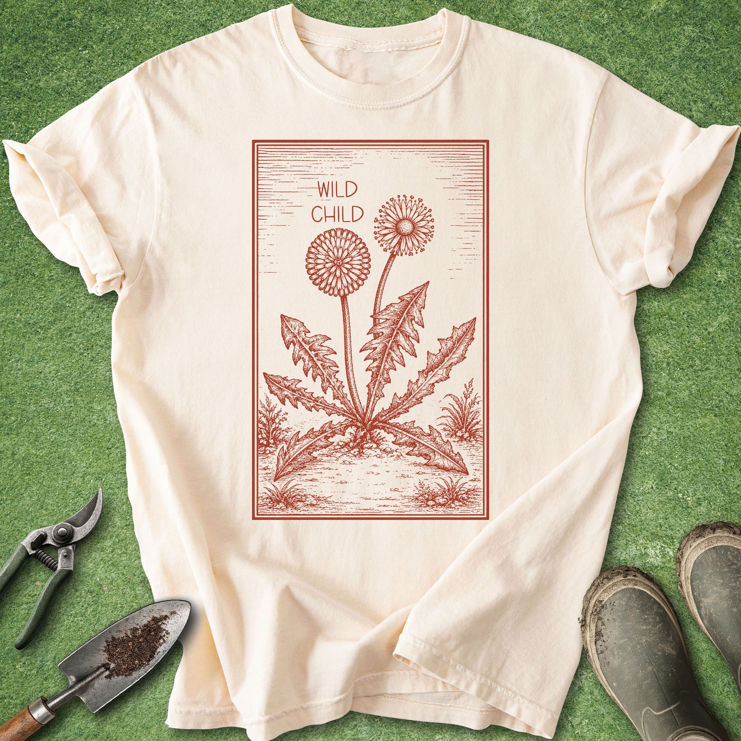 Beige t-shirt with red dandelion graphic and 'Wild Child' text on a green grass background.