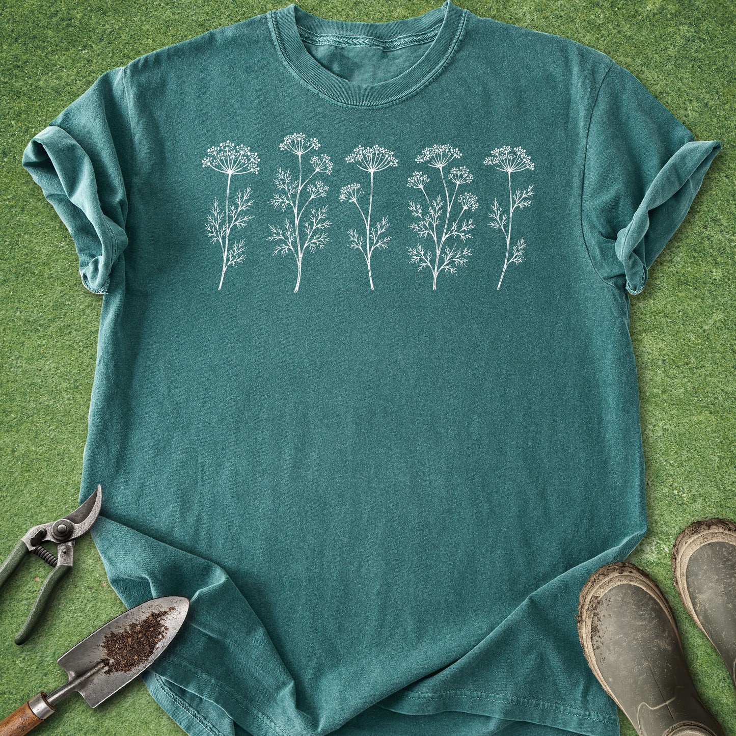 Teal t-shirt with white floral design on a green grass background