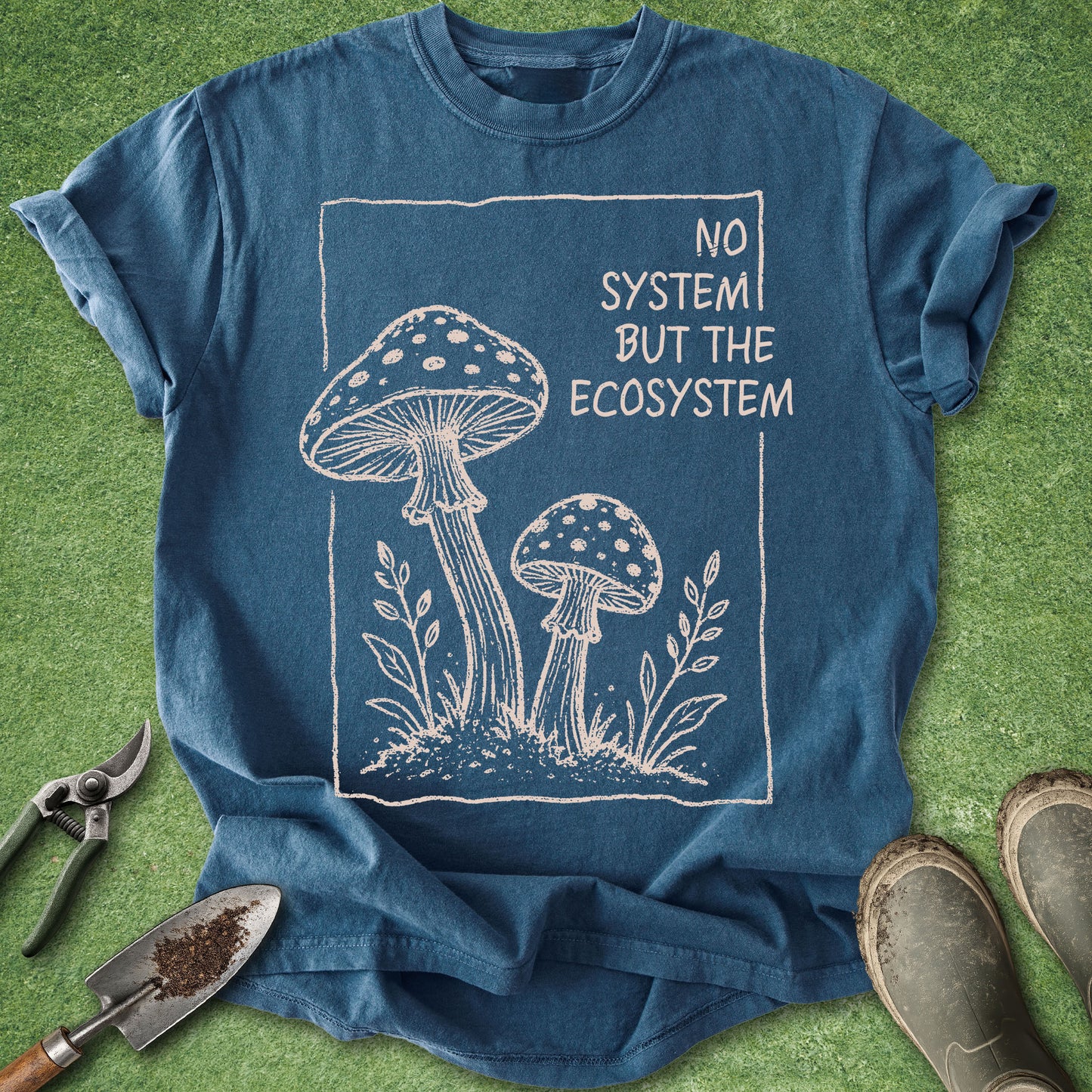 Blue t-shirt with mushroom design and 'No System But The Ecosystem' text on a grass background