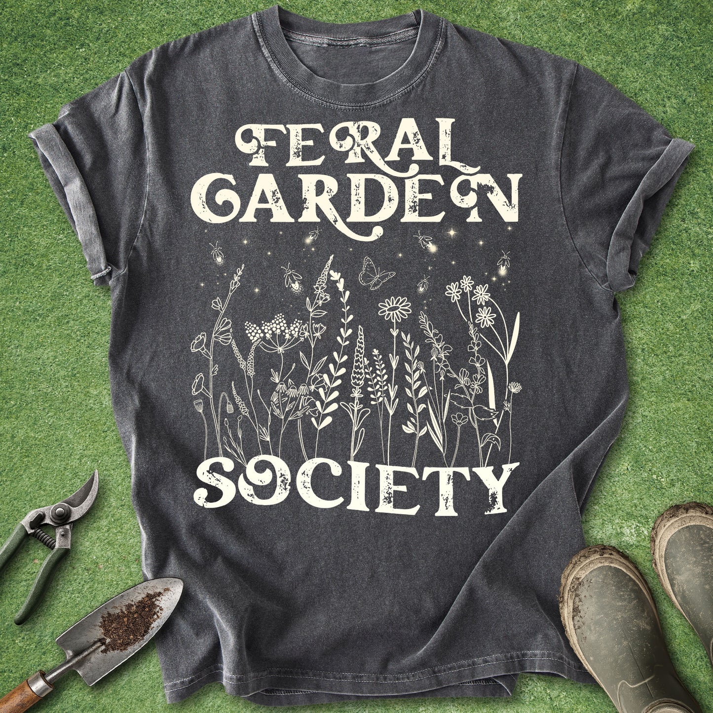Vintage botanical gardening shirt featuring the words "Feral Garden Society" with delicate wildflowers, butterflies, and glowing fireflies on a dark charcoal background.
