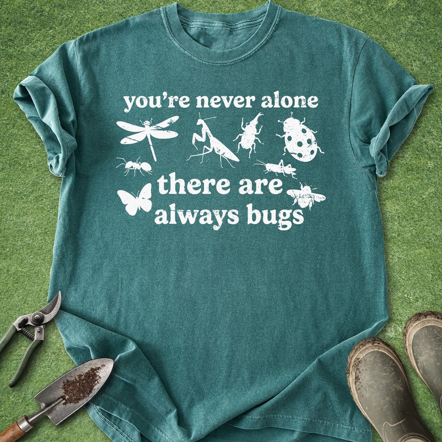 Blue Spruce Comfort Colors t-shirt featuring the phrase "You're Never Alone There Are Always Bugs" surrounded by silhouettes of garden insects including a dragonfly, ladybug, praying mantis, butterfly, bee, ant, and beetle.