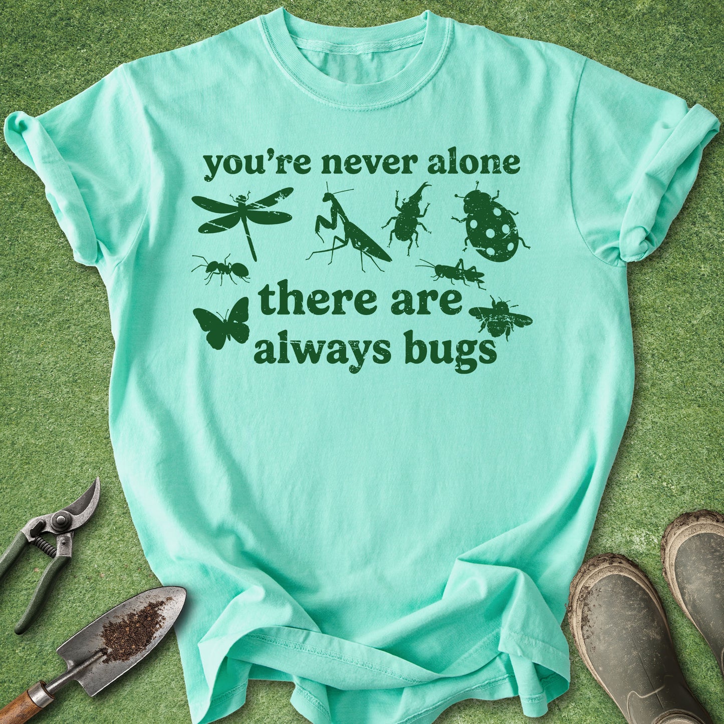 Mint green t-shirt with insect illustrations and text on a grass background