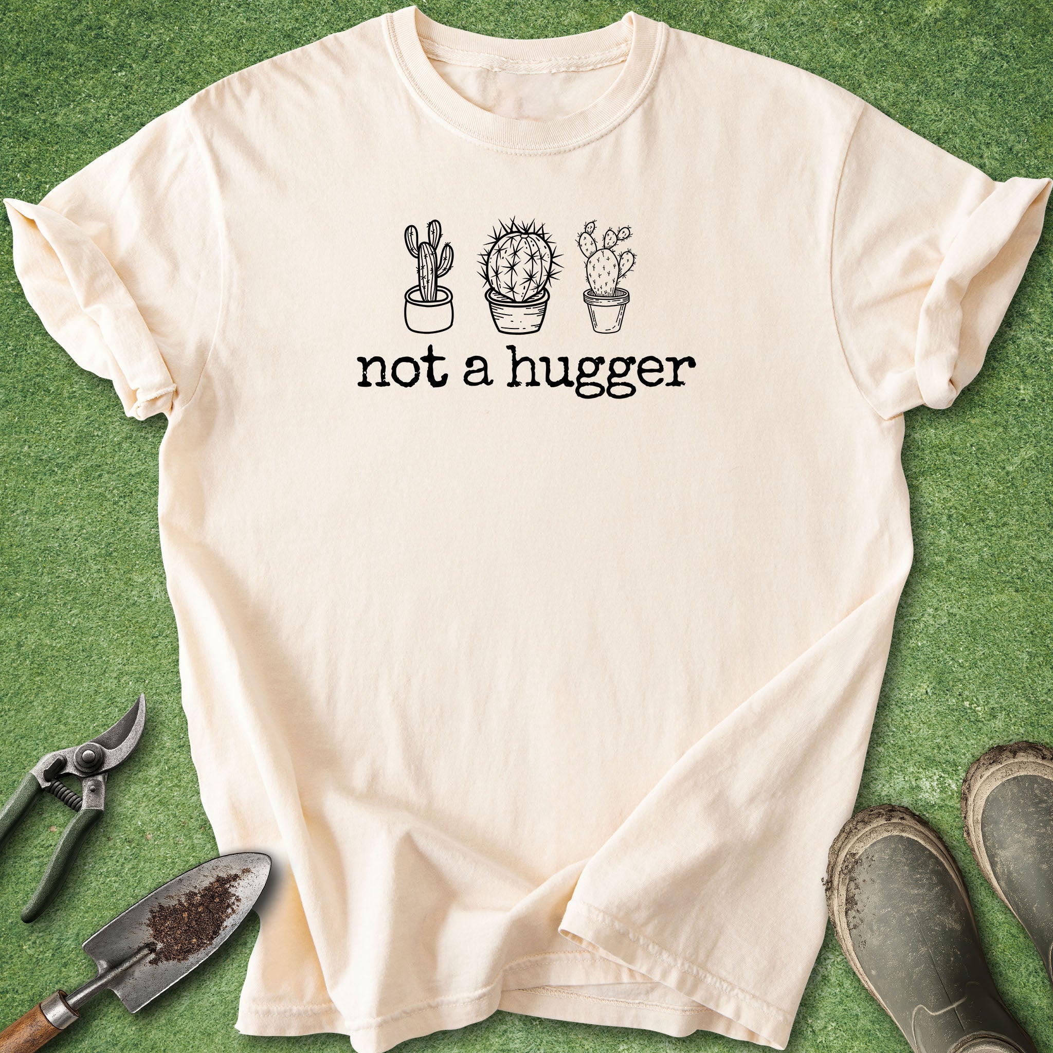 Beige t-shirt with cactus design and 'not a hugger' text on a green grass background