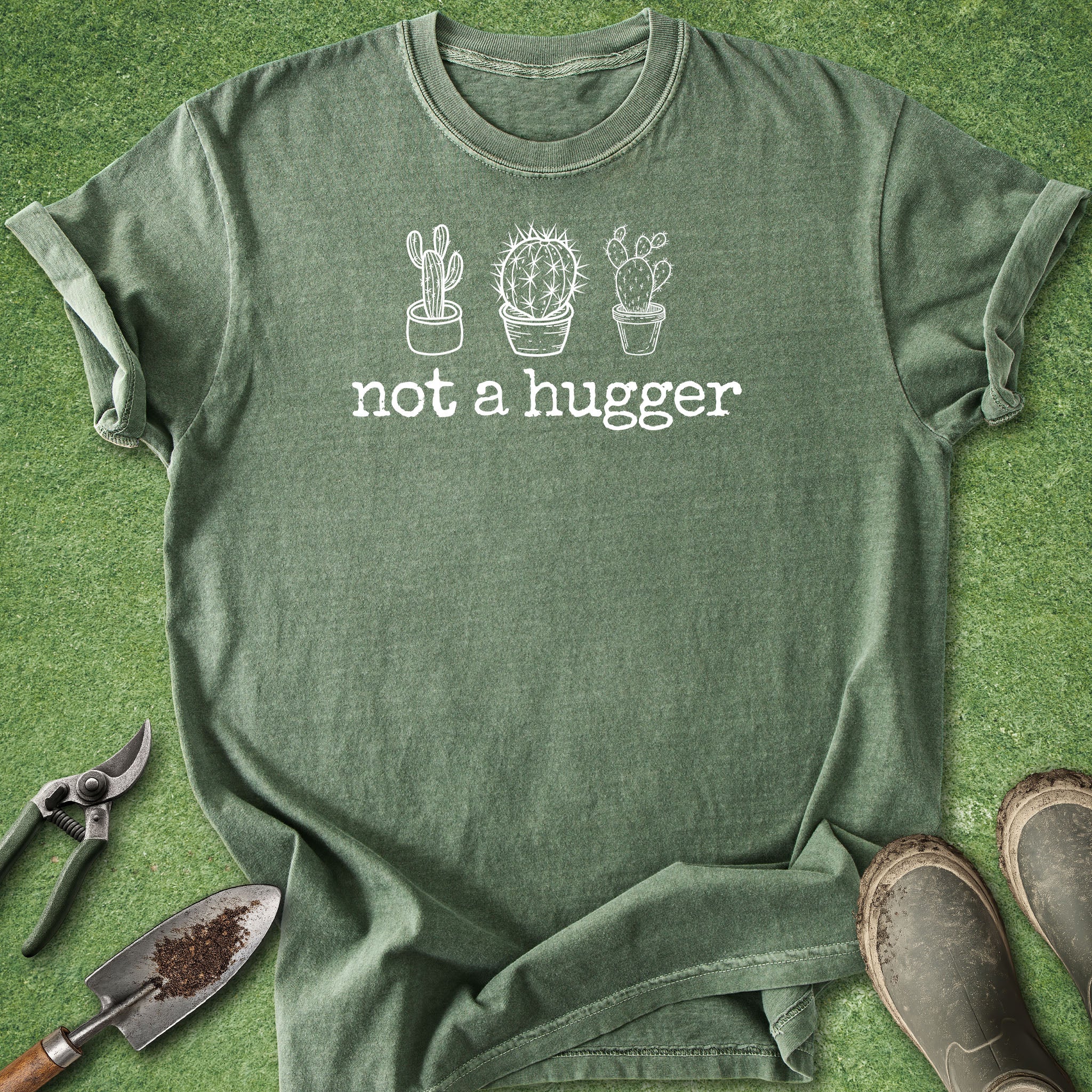 Green t-shirt with cactus design and 'not a hugger' text on a grass background