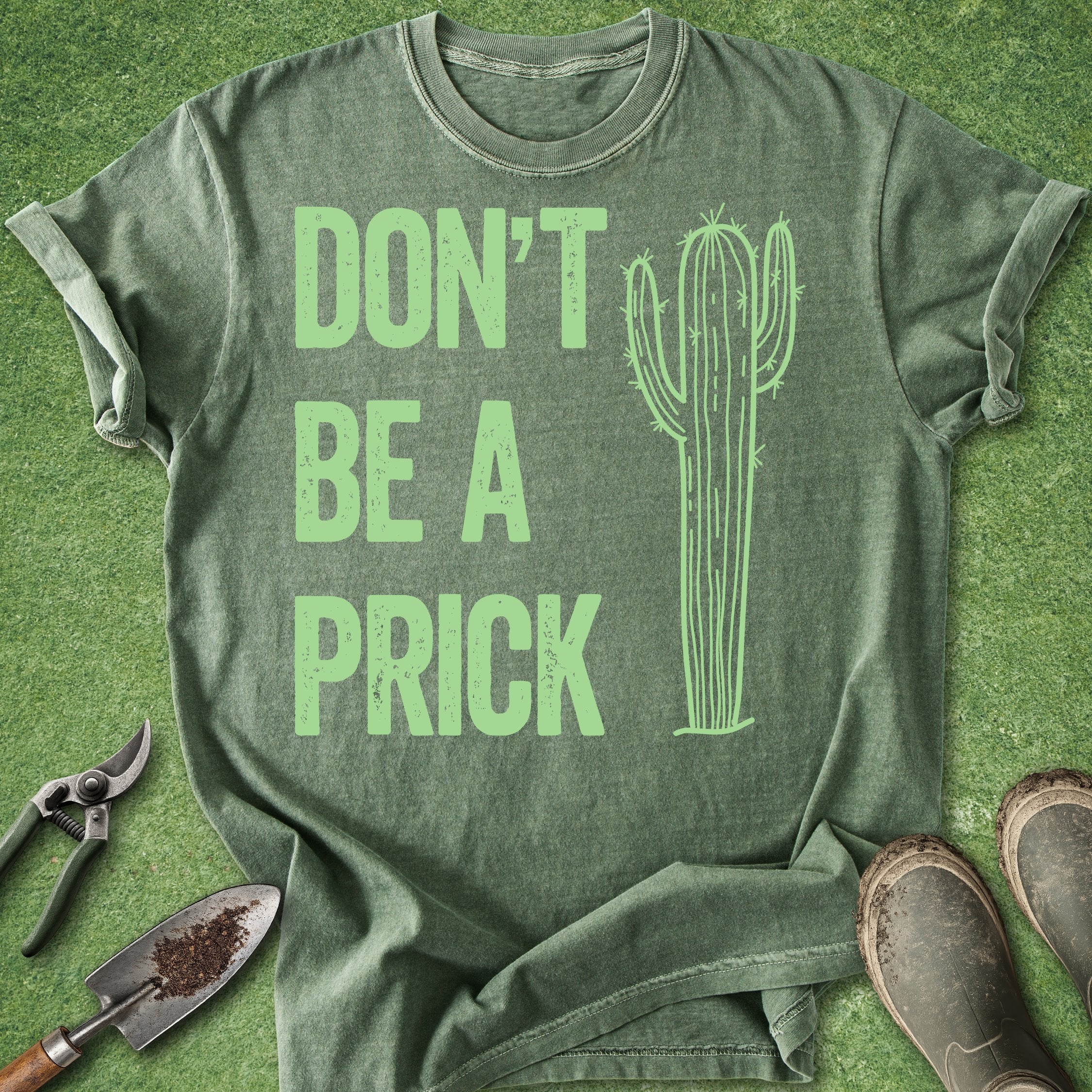 Green t-shirt with 'DON'T BE A PRICK' text and cactus graphic on a grass background