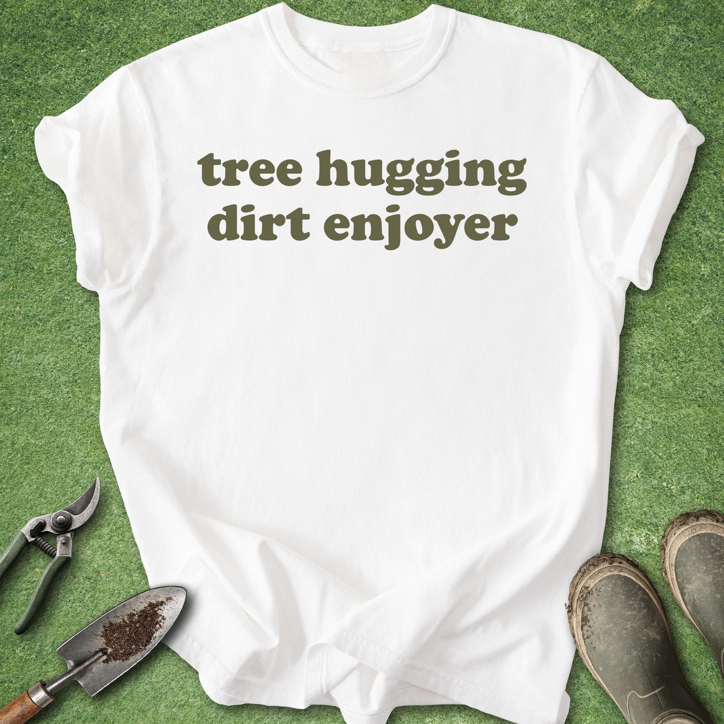 White t-shirt with 'tree hugging dirt enjoyer' text on a green background with gardening tools.