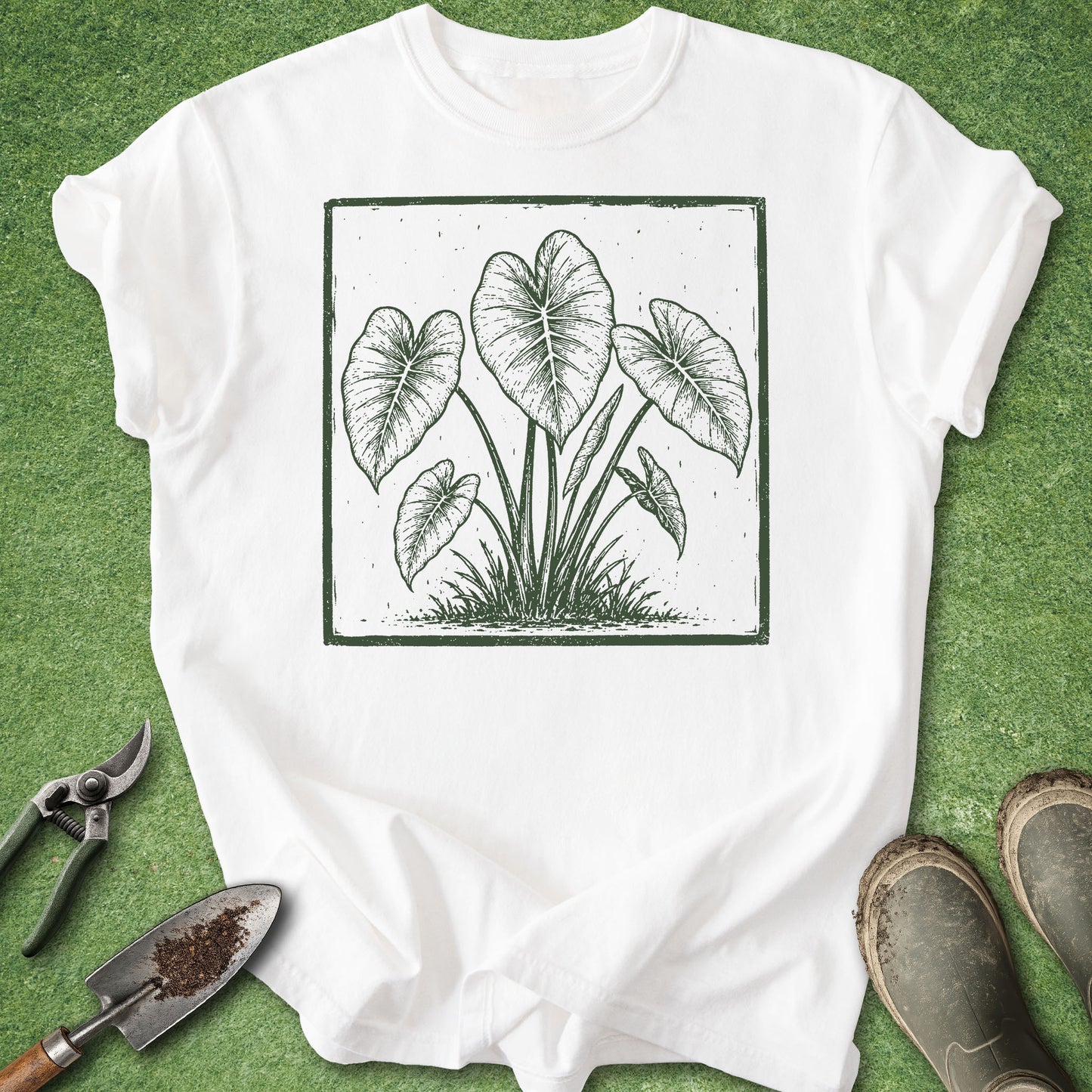 White t-shirt featuring a vintage-style botanical illustration of an Elephant Ear (Alocasia) plant with large heart-shaped leaves inside a distressed square frame.