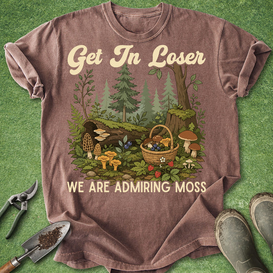 Comfort Colors espresso t-shirt featuring the phrase "Get In Loser We're Admiring Moss" with a detailed woodland scene including mushrooms, moss, ferns, berries, trees, and a foraging basket.