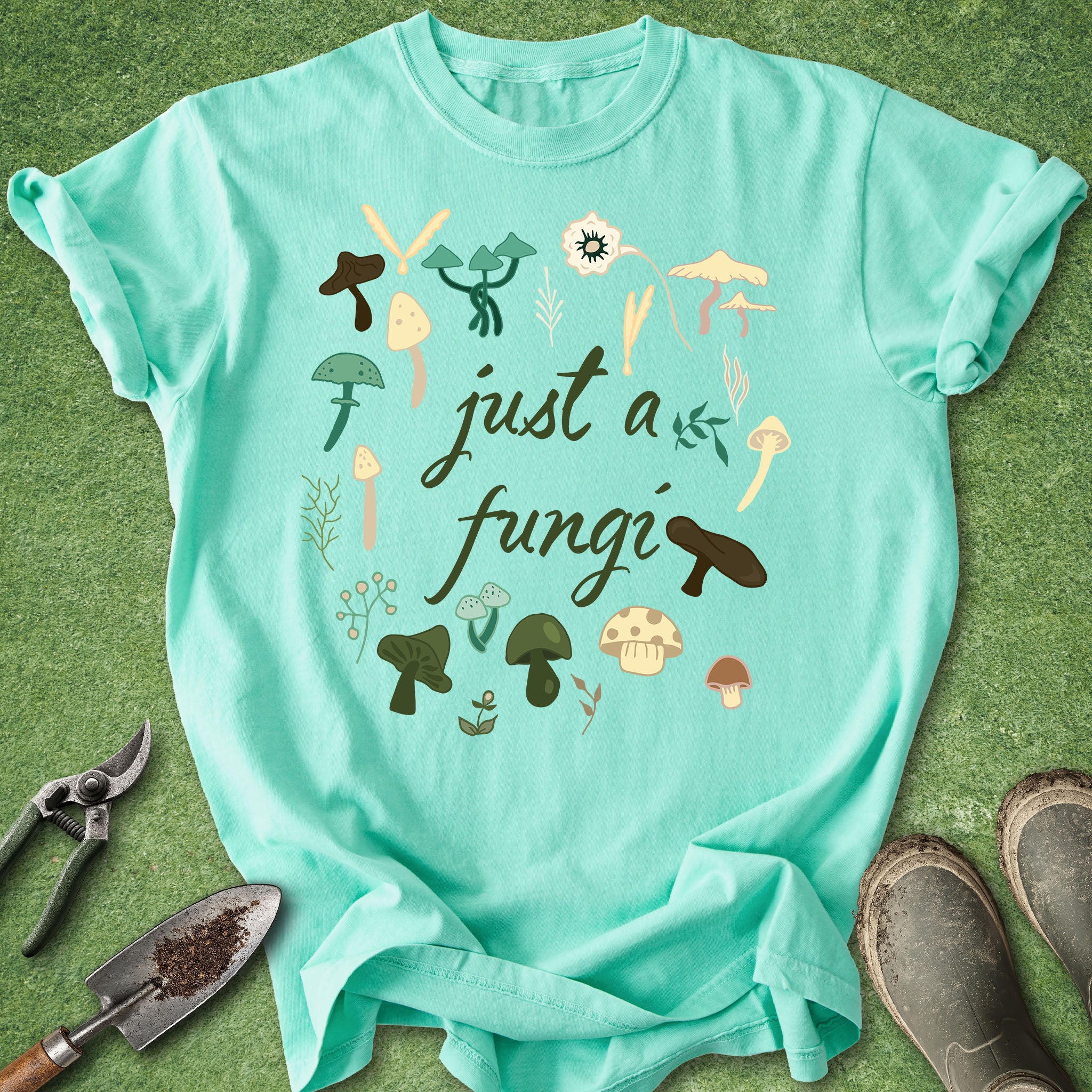 Mint green t-shirt with mushroom illustrations and text on a grass background