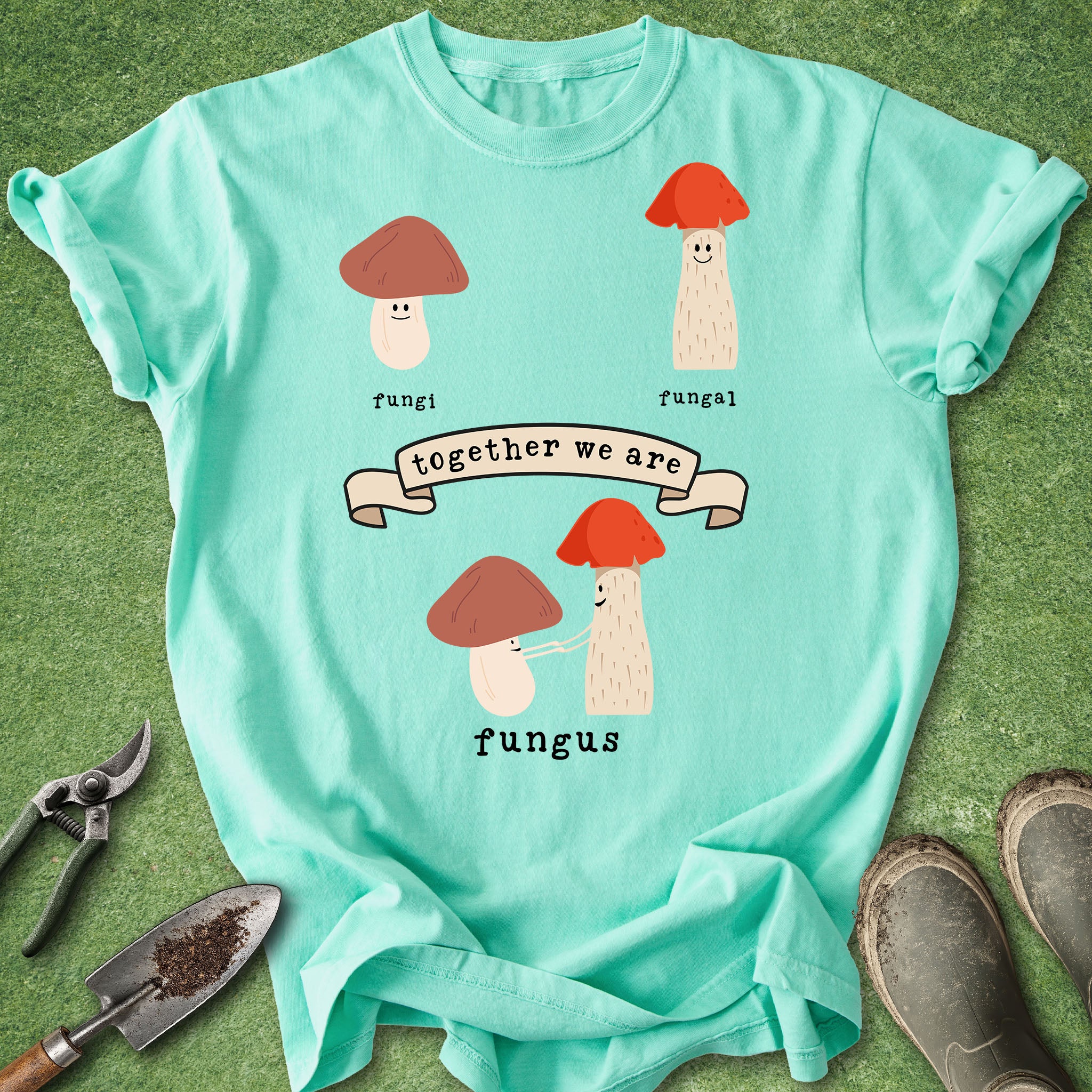 Light blue t-shirt with cartoon mushrooms and text on a green grass background
