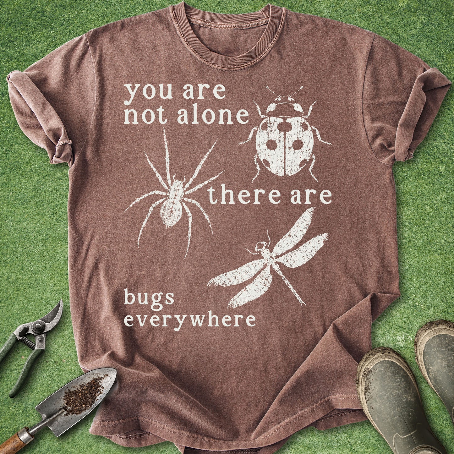 Brown t-shirt with white text and insect illustrations on a green grass background