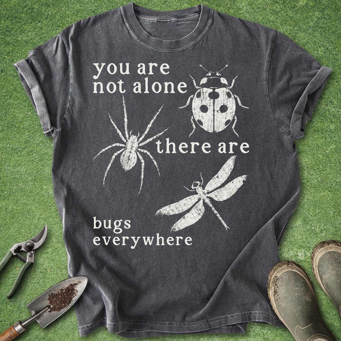 Dark gray t-shirt with white text and insect illustrations on a green grass background.