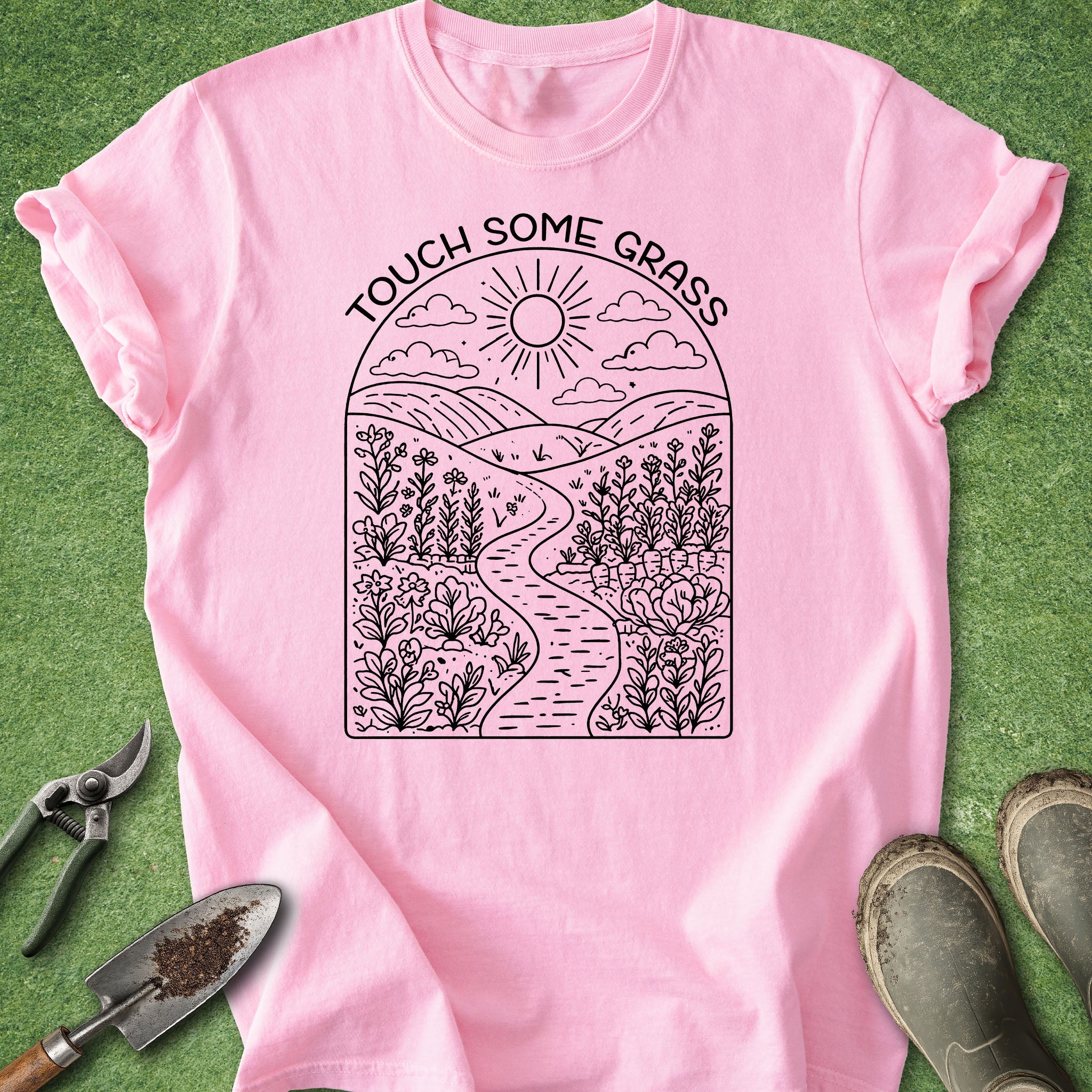 Pink t-shirt with nature-themed design and text 'Touch Some Grass' on a grass background.
