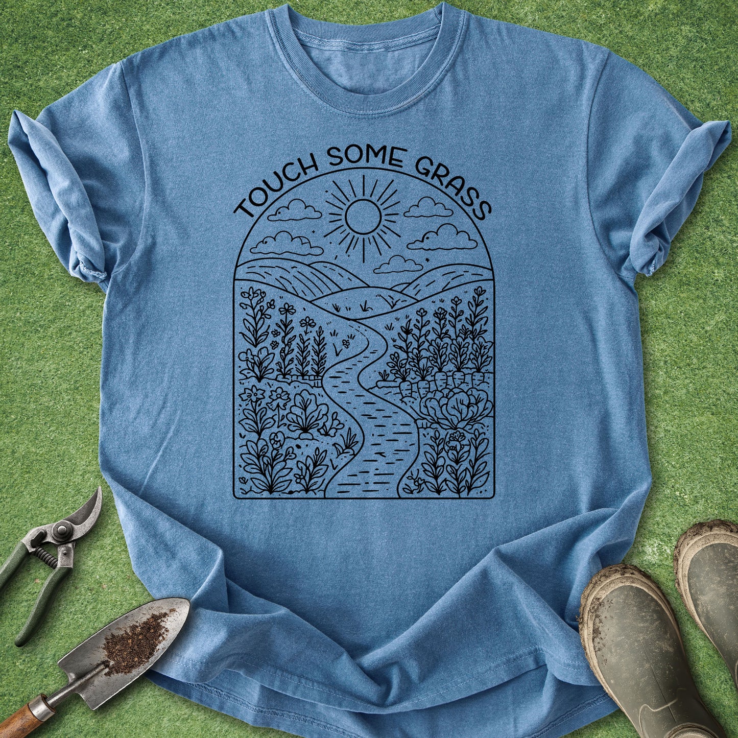 Blue t-shirt with nature-themed design and gardening tools on a grass background