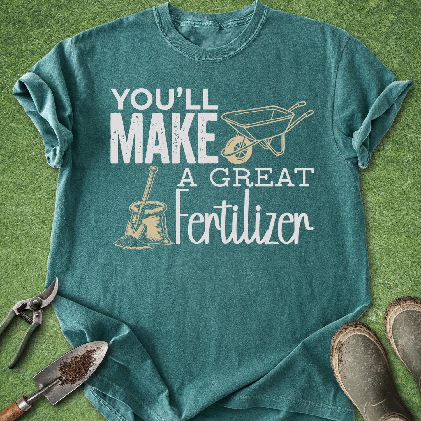 Teal t-shirt with gardening-themed text and graphics on a grass background