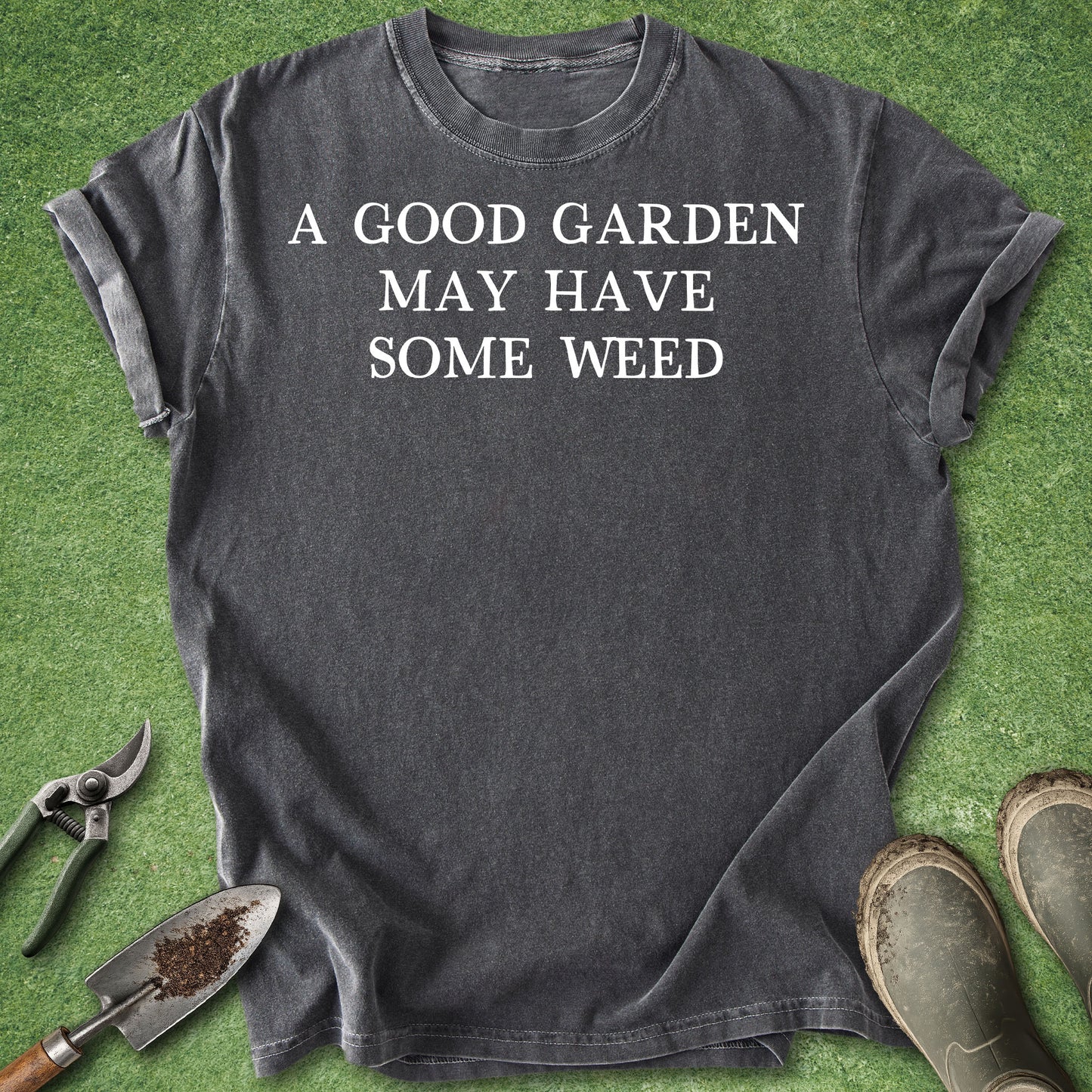 Gray t-shirt with 'A good garden may have some weed' text on a grass background with gardening tools.