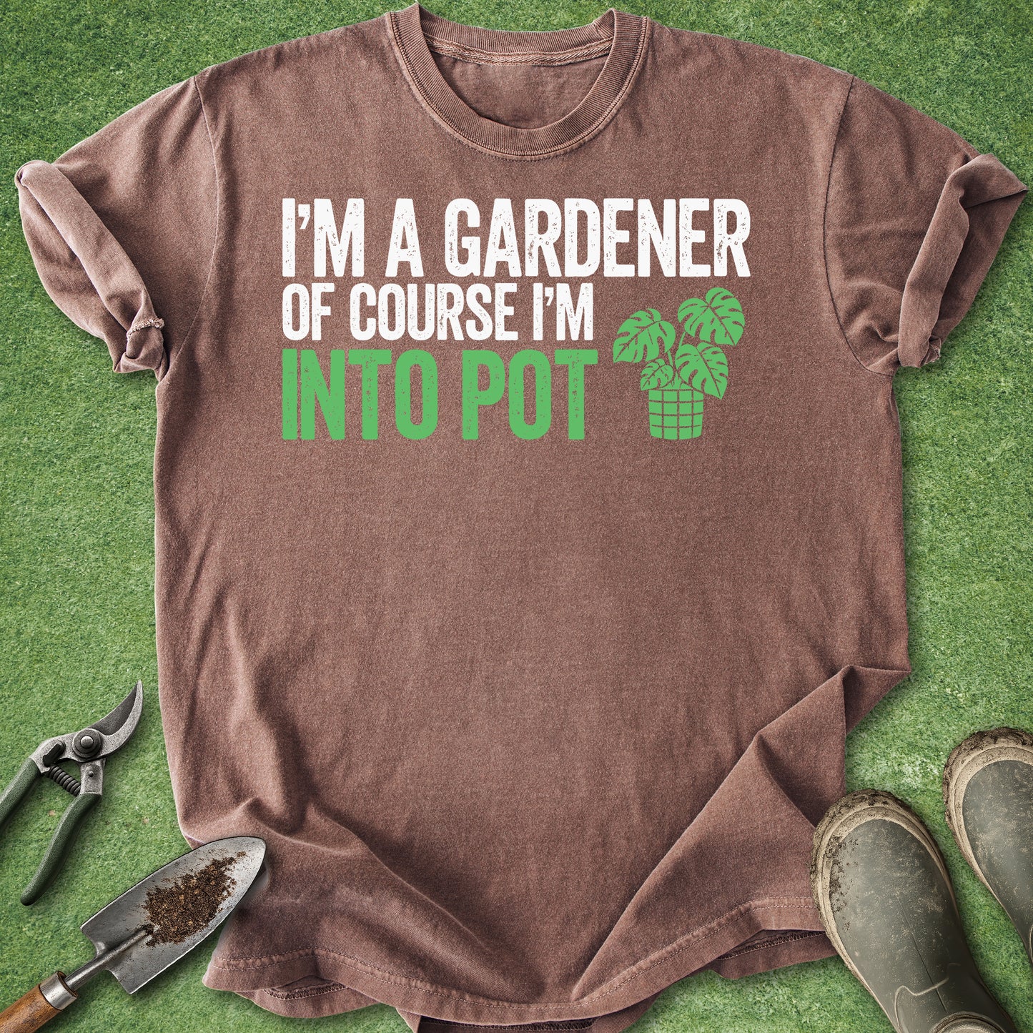 Brown t-shirt with humorous gardening text on a green background with gardening tools.