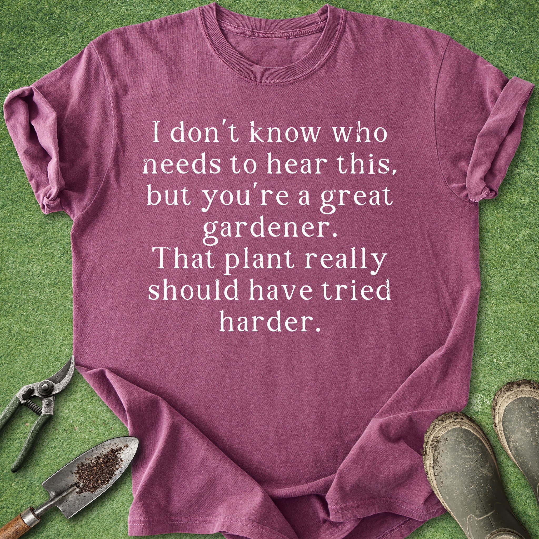 Purple t-shirt with humorous gardening text on a green background with gardening tools.