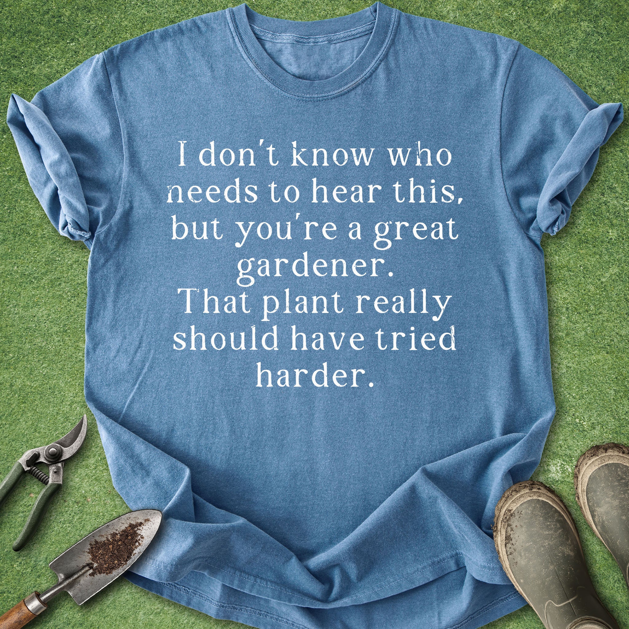 Blue t-shirt with humorous gardening text on a grass background with gardening tools.
