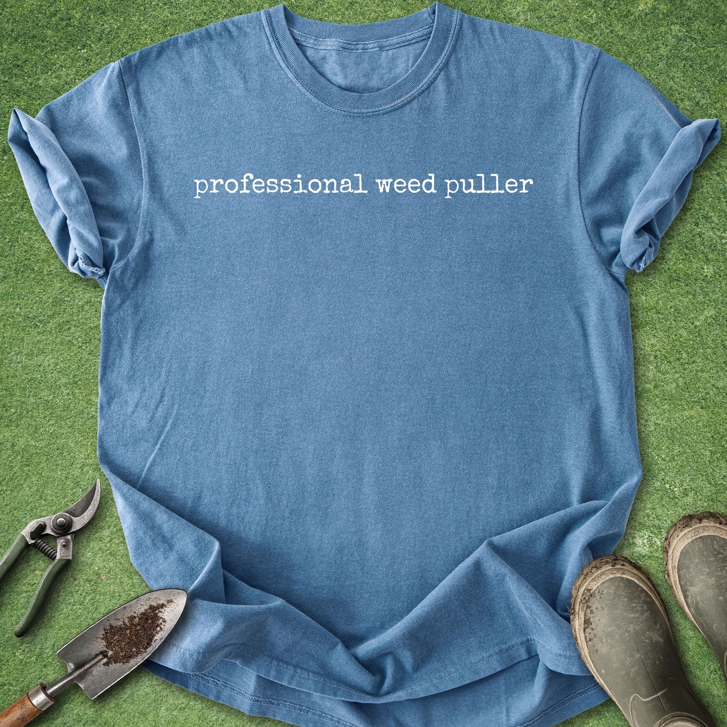 Blue t-shirt with 'professional weed puller' text on a grass background with gardening tools.