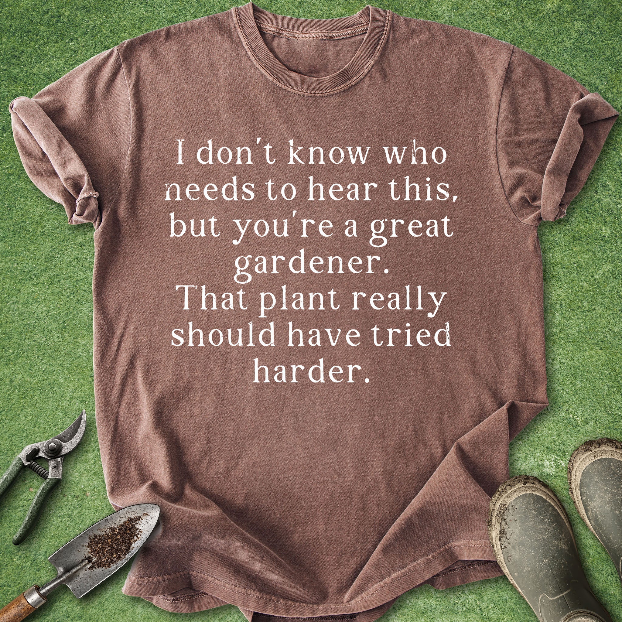 Brown t-shirt with humorous gardening text on a green background with gardening tools.