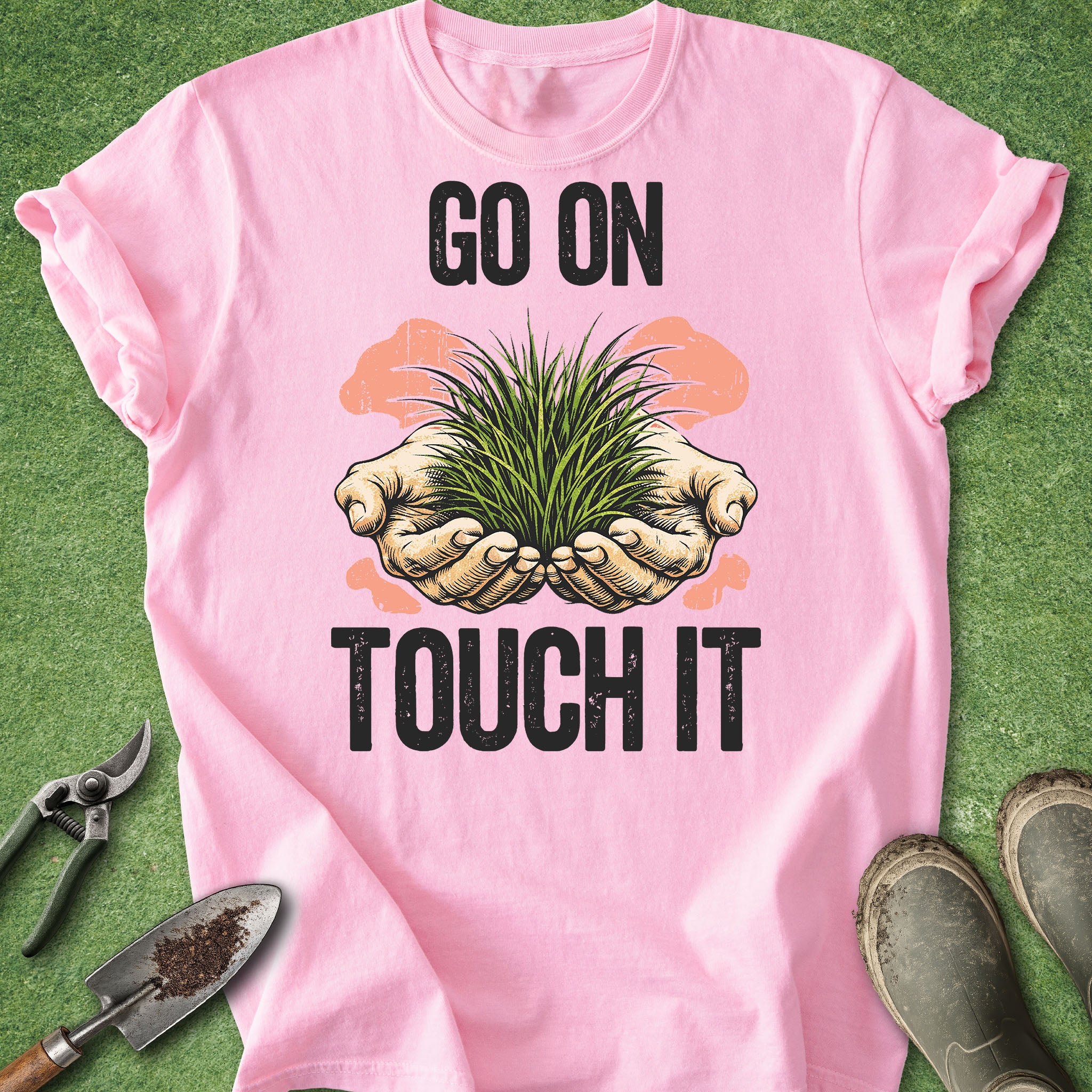 Pink t-shirt with 'Go on, touch it' graphic and gardening tools on a green background