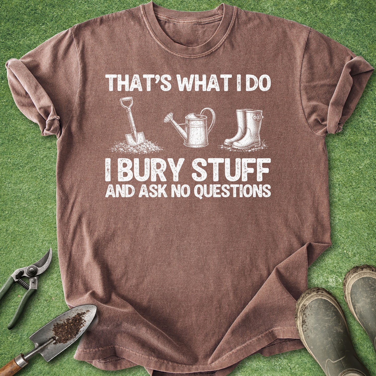 Brown Comfort Colors t-shirt featuring the funny quote "That's What I Do I Bury Stuff and Ask No Questions" with vintage-style illustrations of a shovel, watering can, and gardening boots.