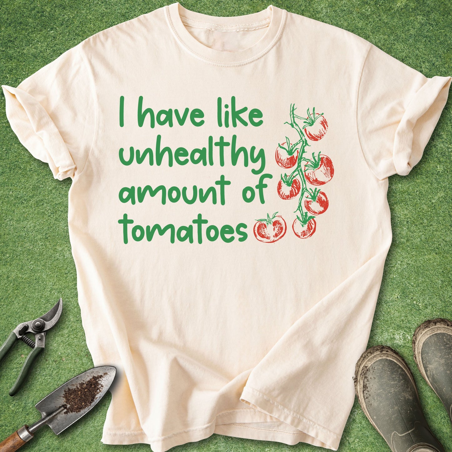 Beige t-shirt with green text and tomato graphics on a green background with gardening tools.