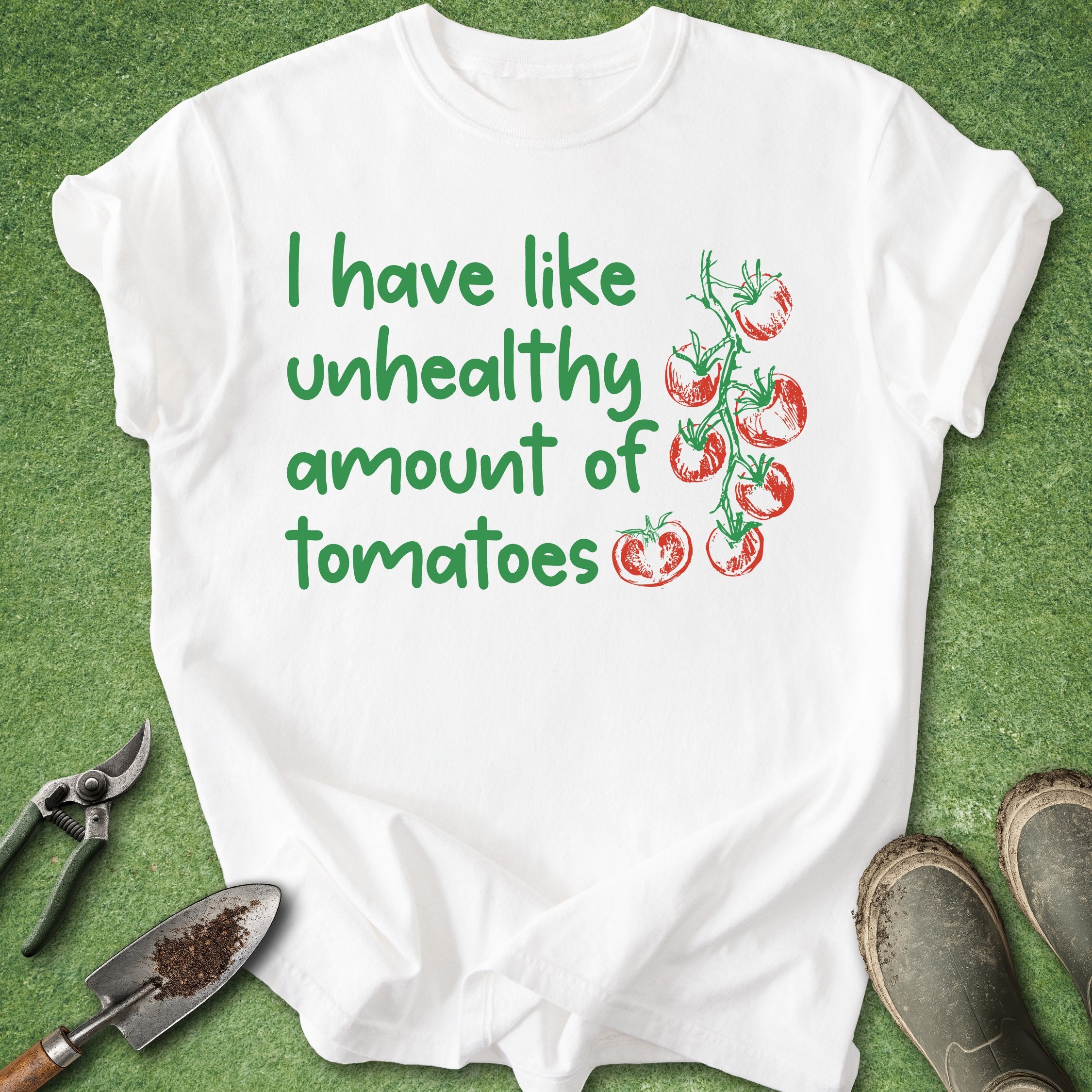 White t-shirt with green text and tomato graphics on a green background with gardening tools.