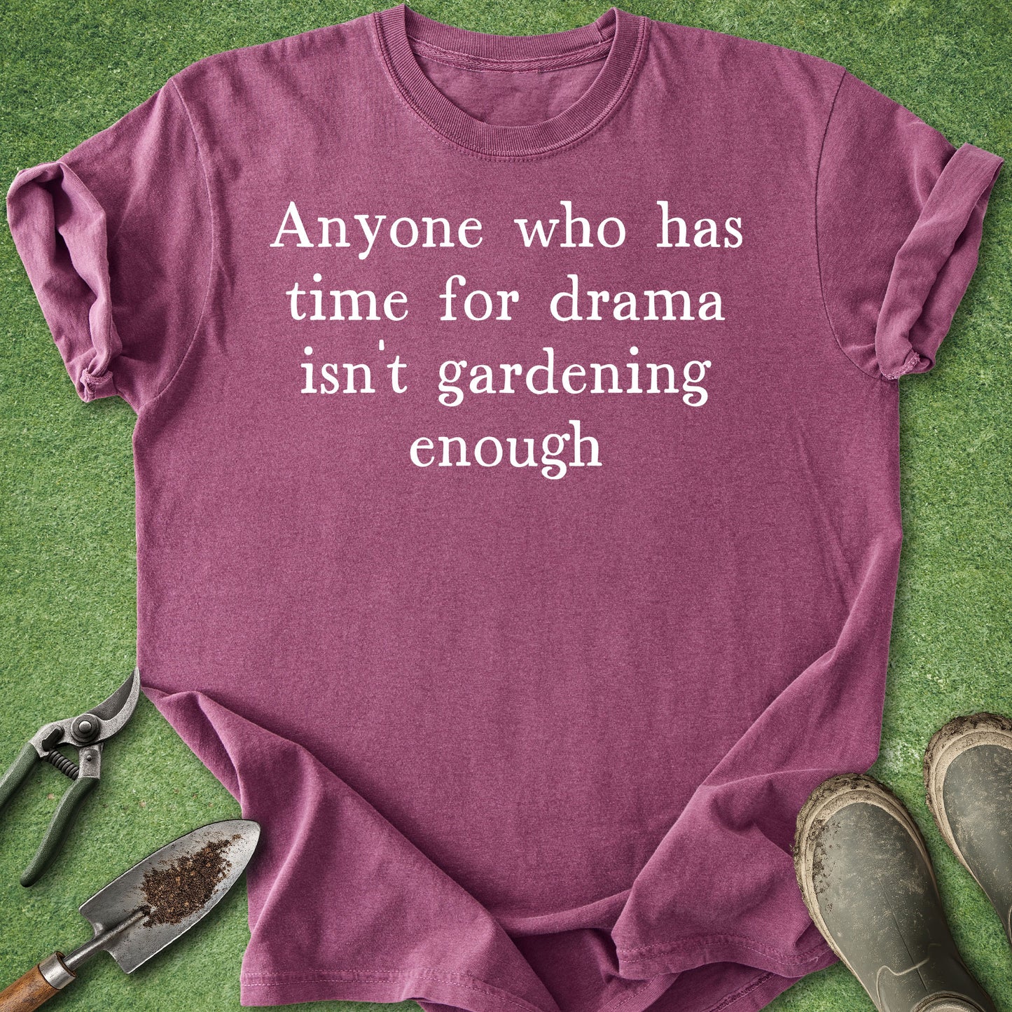 Purple t-shirt with humorous text on a grass background with gardening tools.