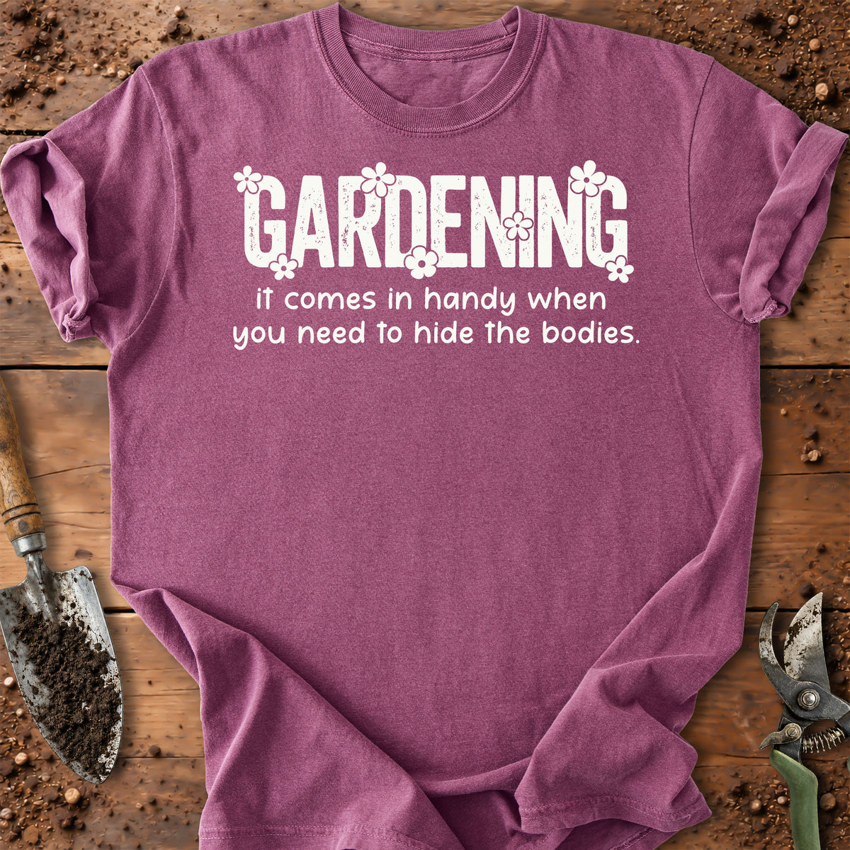 A heathered purple short-sleeve t-shirt with a white graphic text that reads 'GARDENING it comes in handy when you need to hide the bodies.' surrounded by small white flowers.