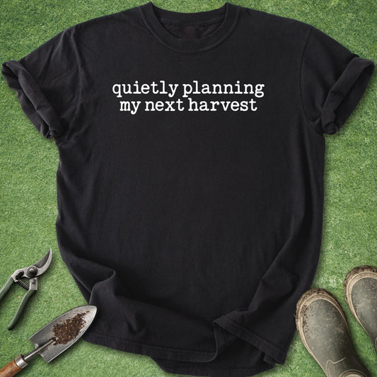 Black t-shirt with 'quietly planning my next harvest' text on a green background with gardening tools.