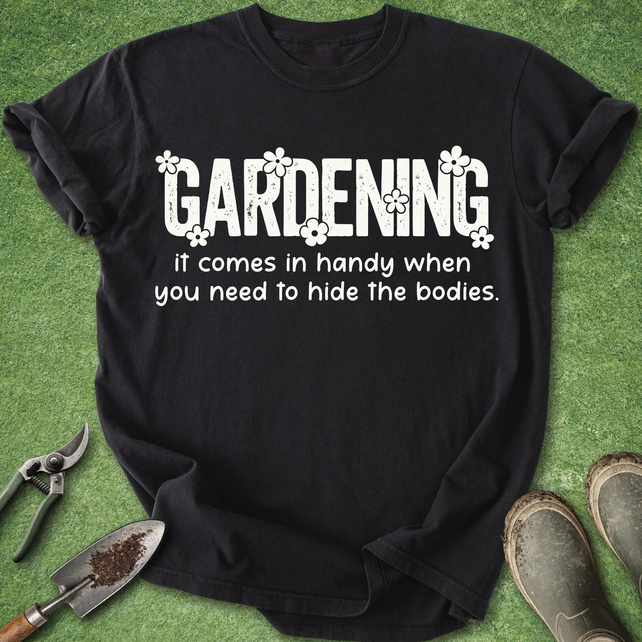 Black t-shirt with humorous gardening text on a green background with gardening tools and boots.