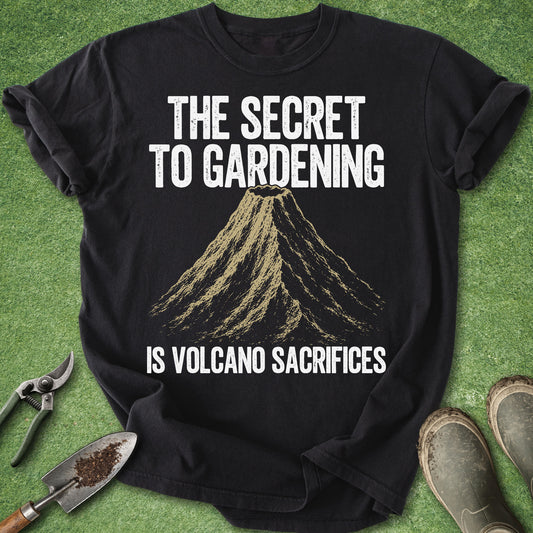 Comfort Colors black t-shirt featuring a vintage volcano illustration with the humorous quote "The Secret to Gardening Is Volcano Sacrifices" in distressed white lettering.