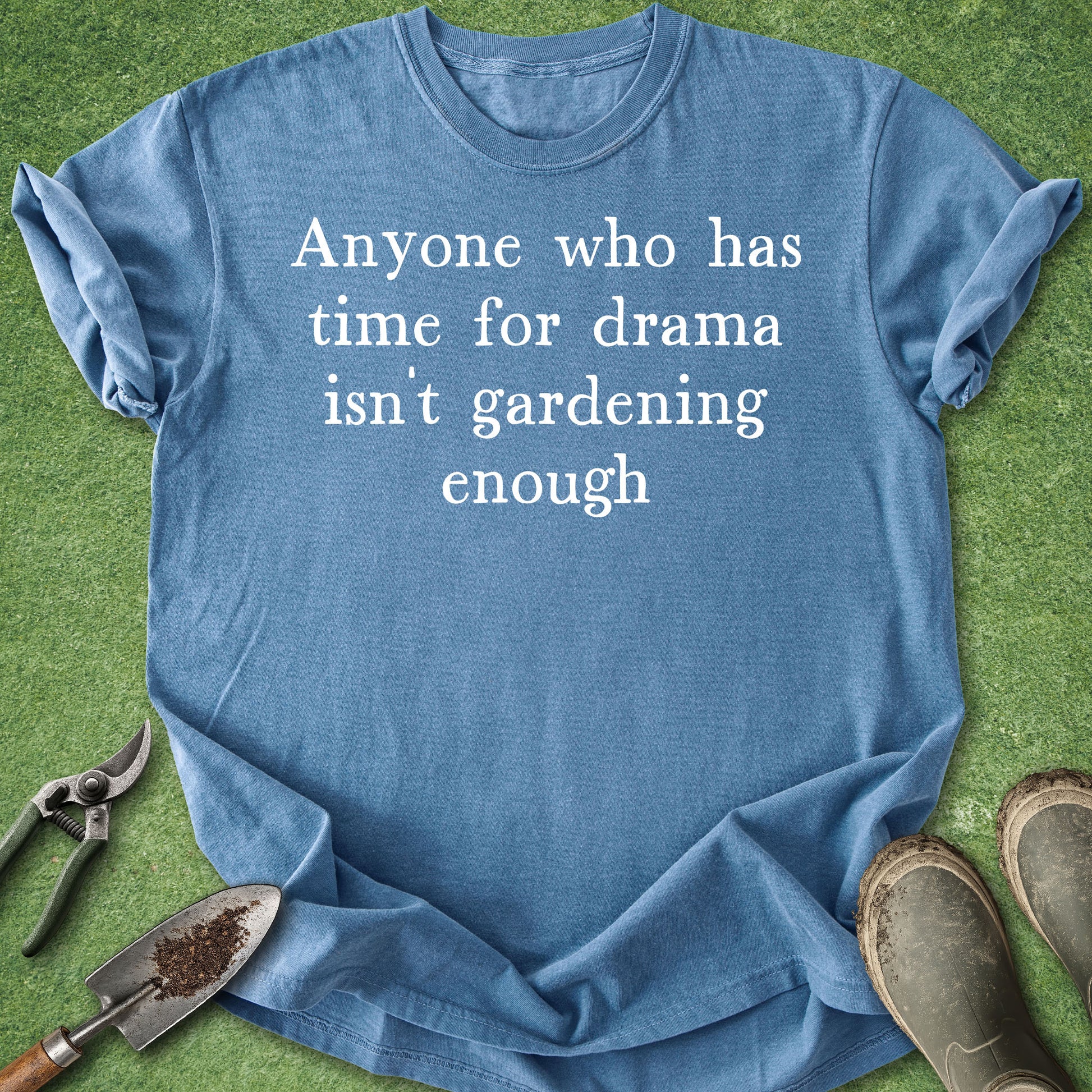 Blue t-shirt with humorous text on a grass background with gardening tools and boots.