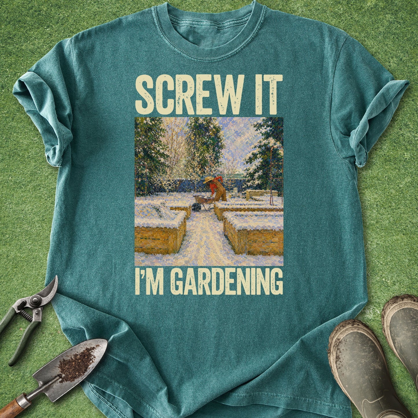 Teal t-shirt with 'Screw it, I'm gardening' text and garden-themed graphic on a grass background.
