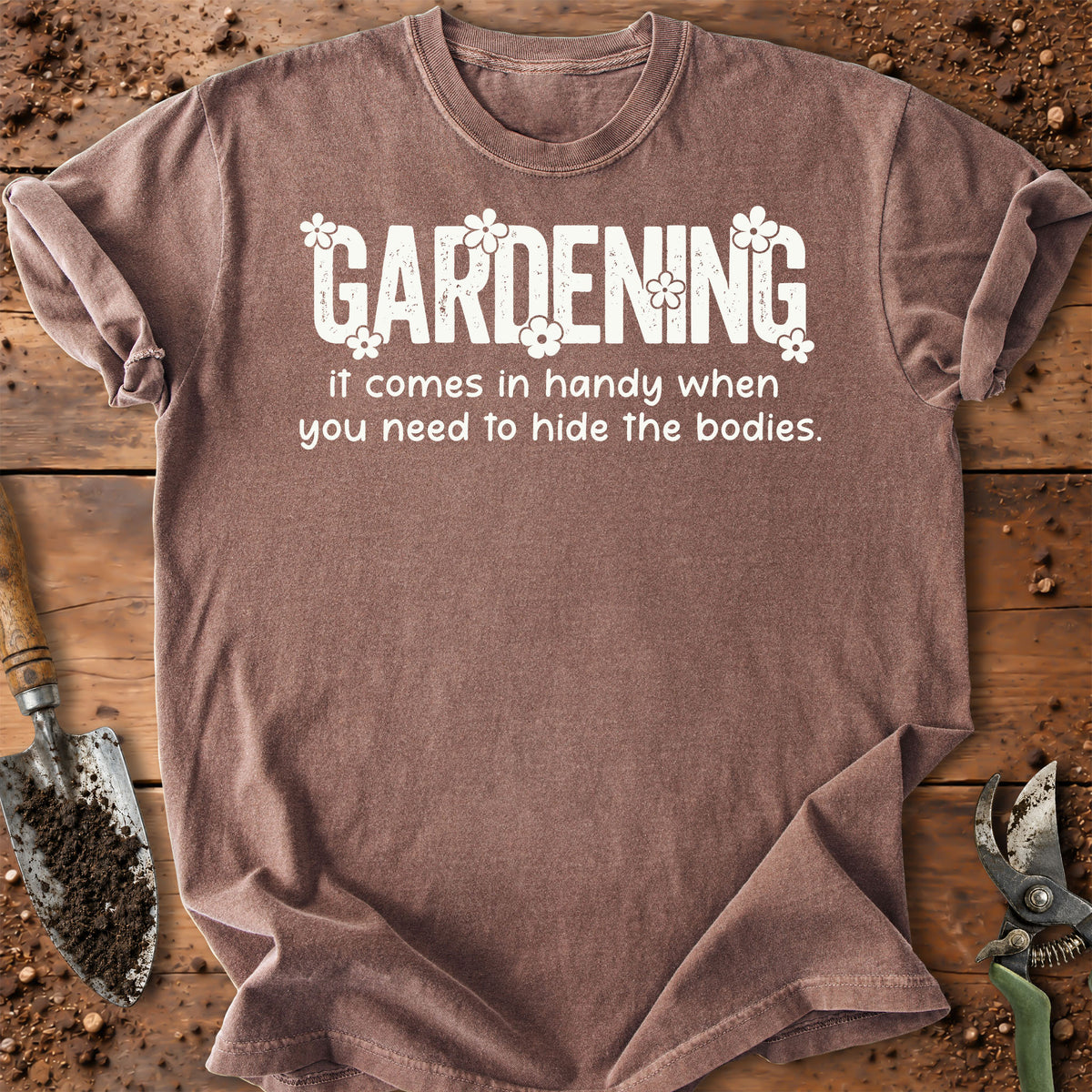 A heathered taupe-brown short-sleeve t-shirt with a white graphic print that reads 'GARDENING it comes in handy when you need to hide the bodies.' in a gardening-themed font.