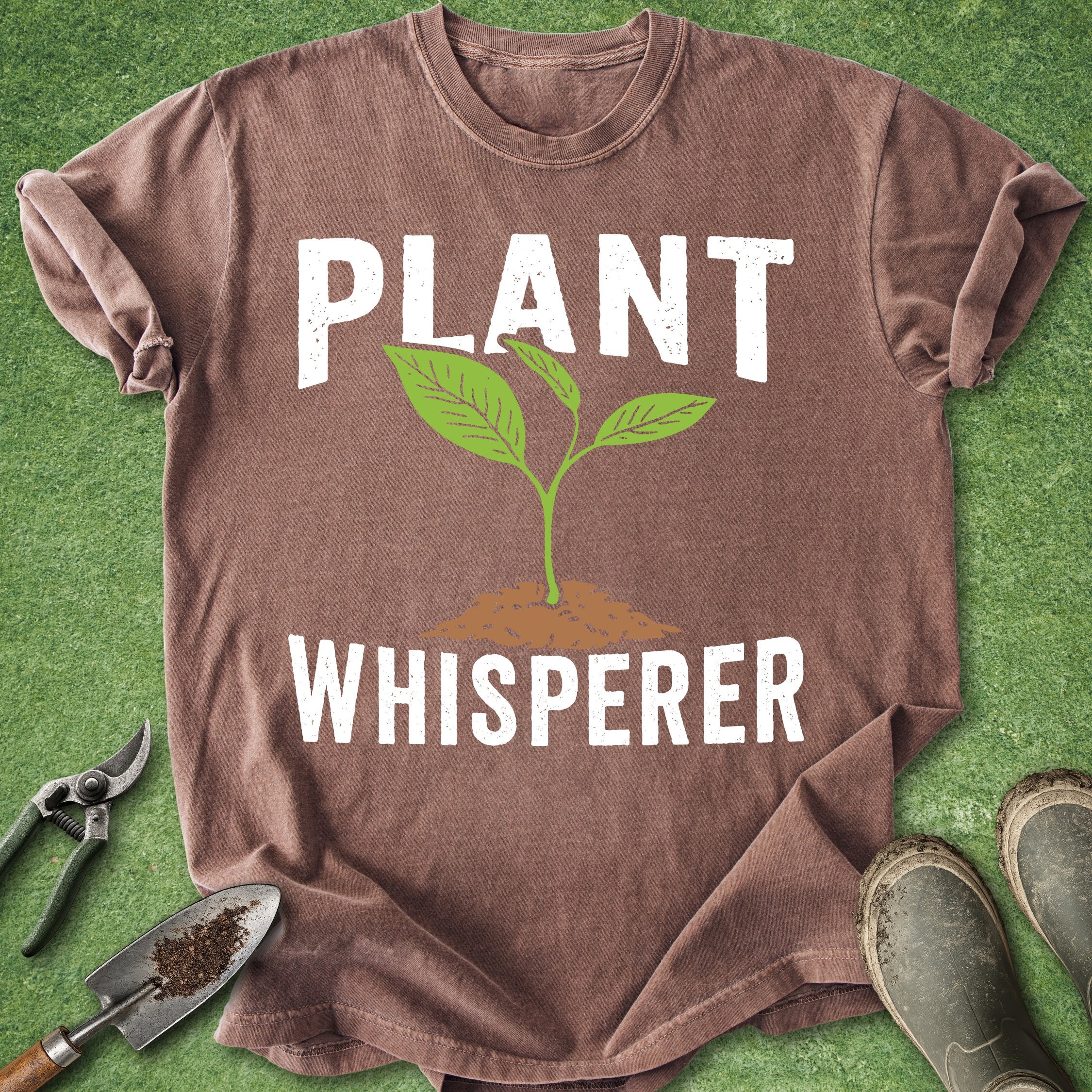 Brown t-shirt with 'Plant Whisperer' text and graphic on a green grass background