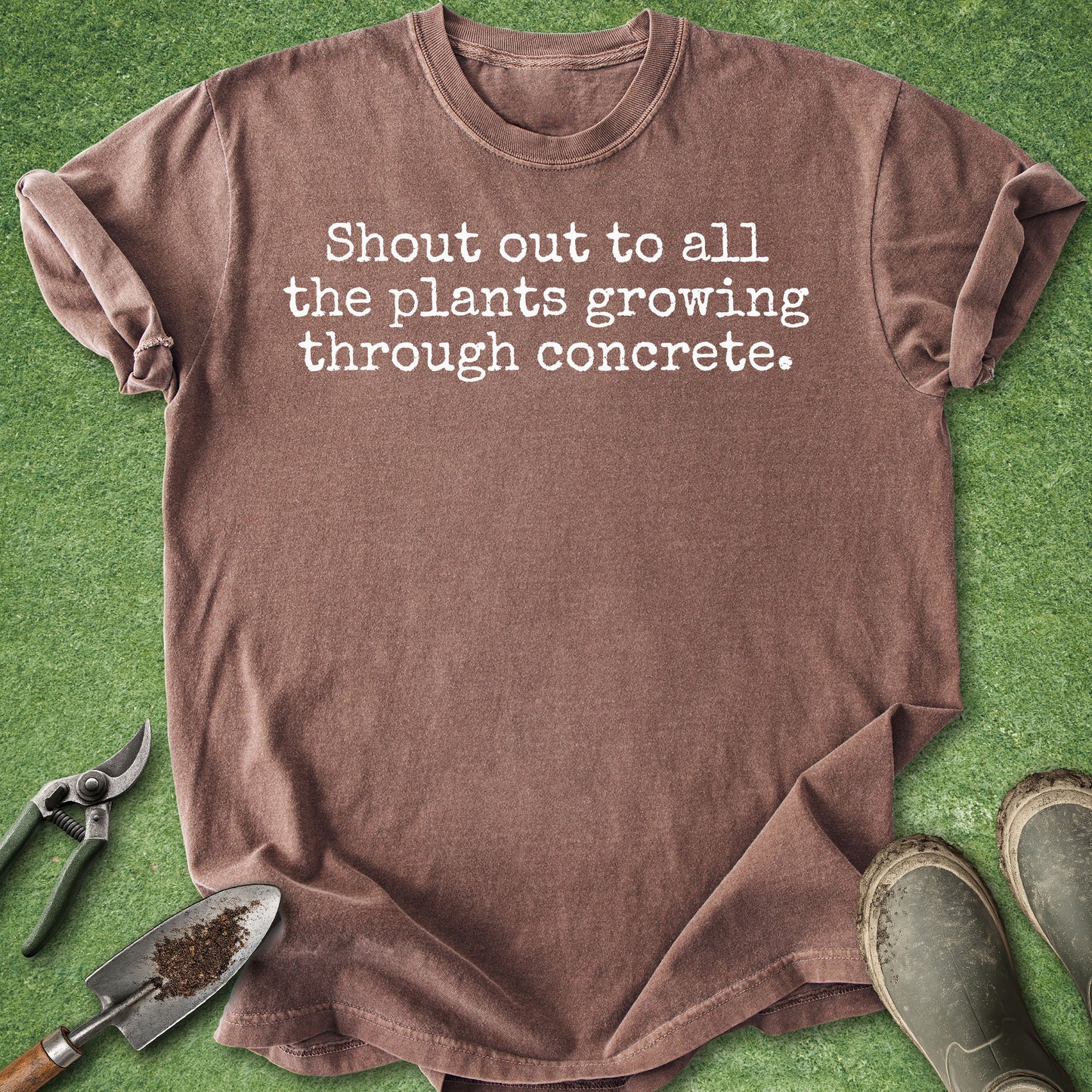 Comfort Colors espresso t-shirt featuring the phrase "Shout out to all the plants growing through concrete." in a minimalist white typewriter-style font.