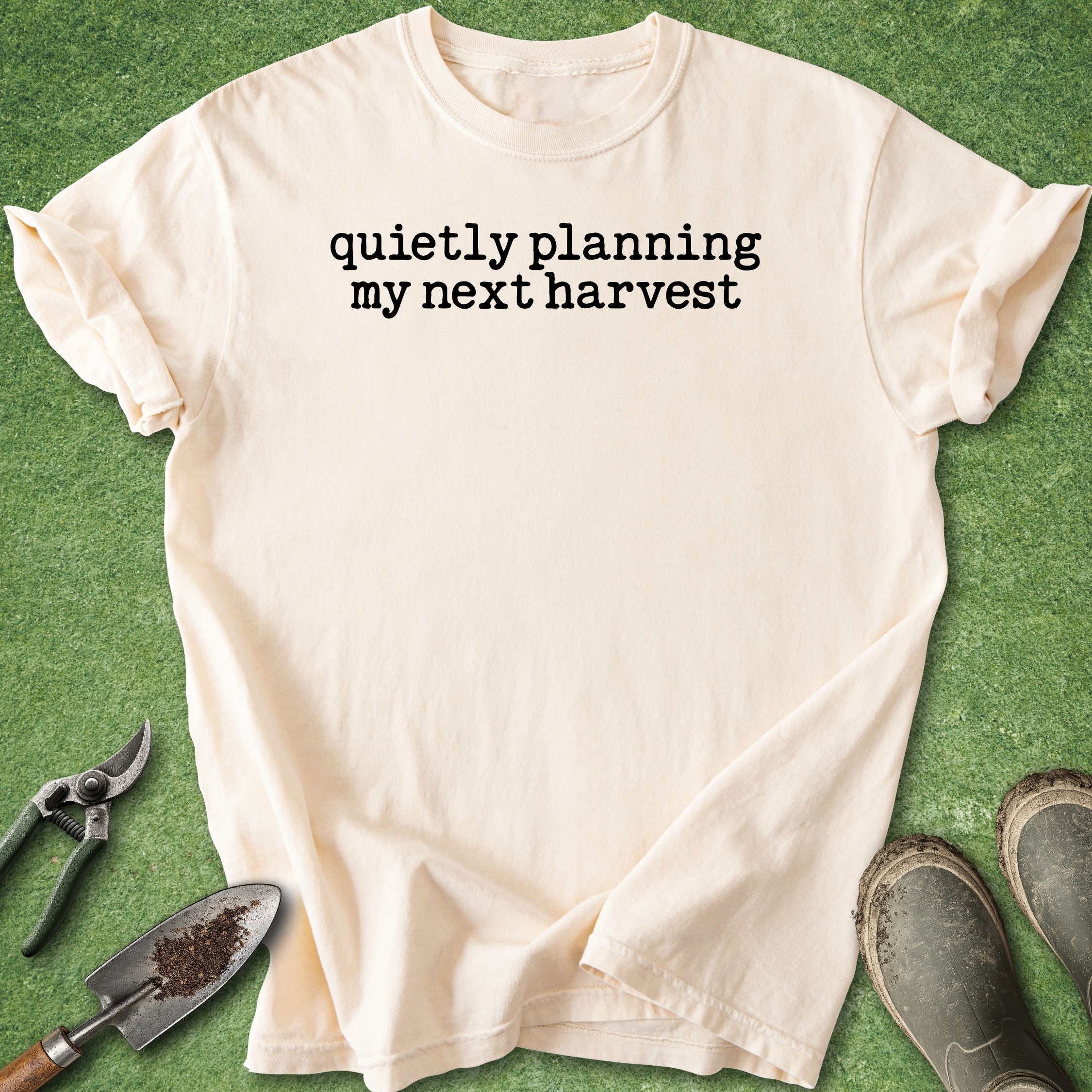 Beige t-shirt with 'quietly planning my next harvest' text on a green background with gardening tools.