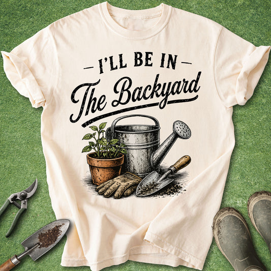 Comfort Colors Ivory t-shirt featuring the quote "I'll Be In The Backyard" with a vintage watering can, potted plant, gardening gloves, and hand trowel illustration.