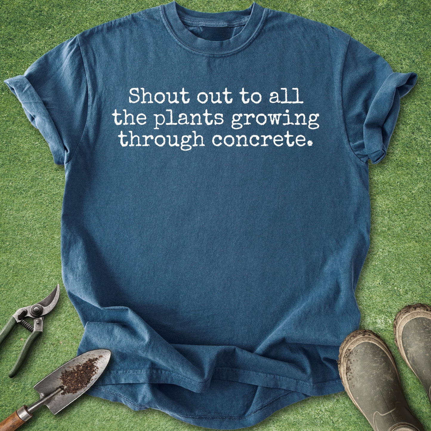 Comfort Colors midnight blue t-shirt featuring the phrase "Shout out to all the plants growing through concrete." in a minimalist white typewriter-style font.