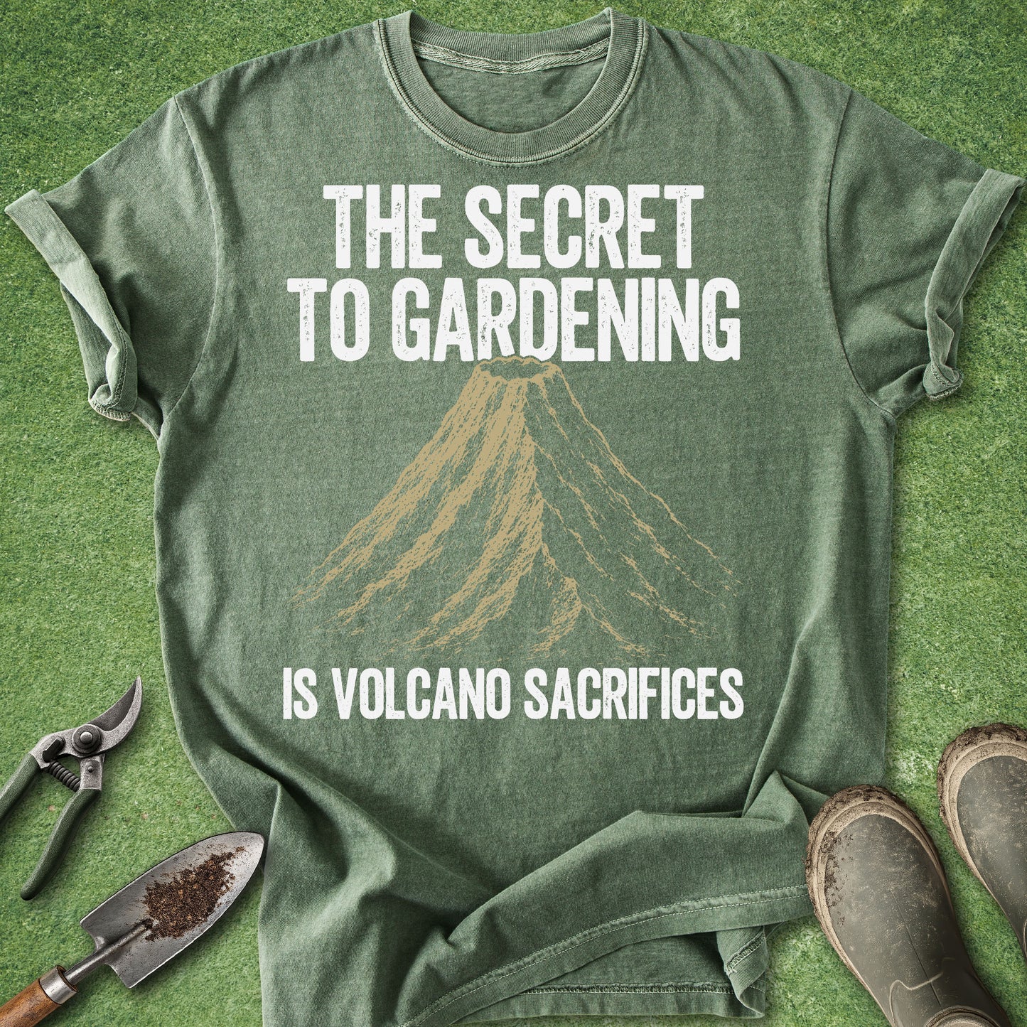 Comfort Colors moss t-shirt featuring a vintage volcano illustration with the humorous quote "The Secret to Gardening Is Volcano Sacrifices" in distressed white lettering.